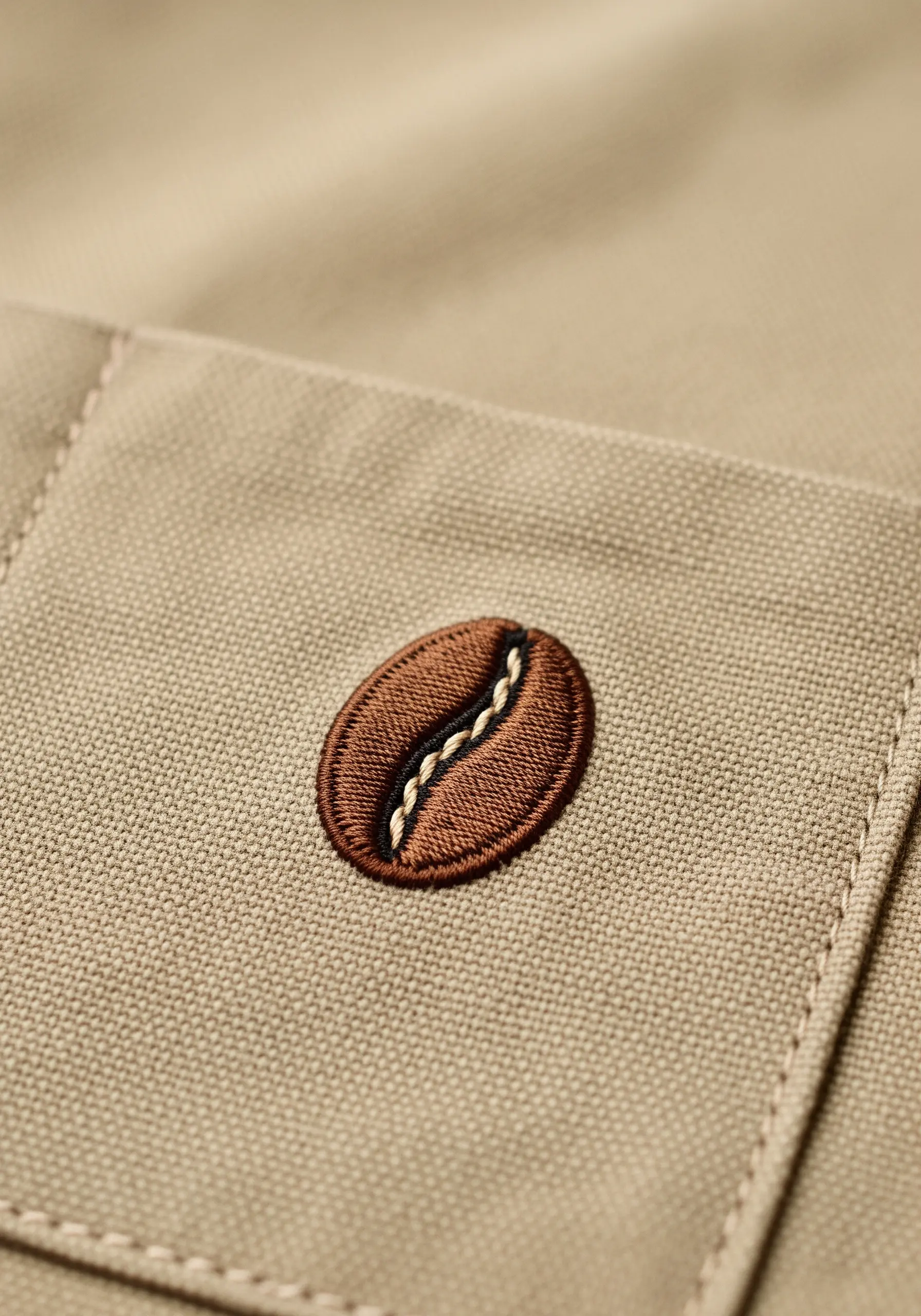 A highly detailed, satin-stitched coffee bean on the pocket of a canvas apron.
