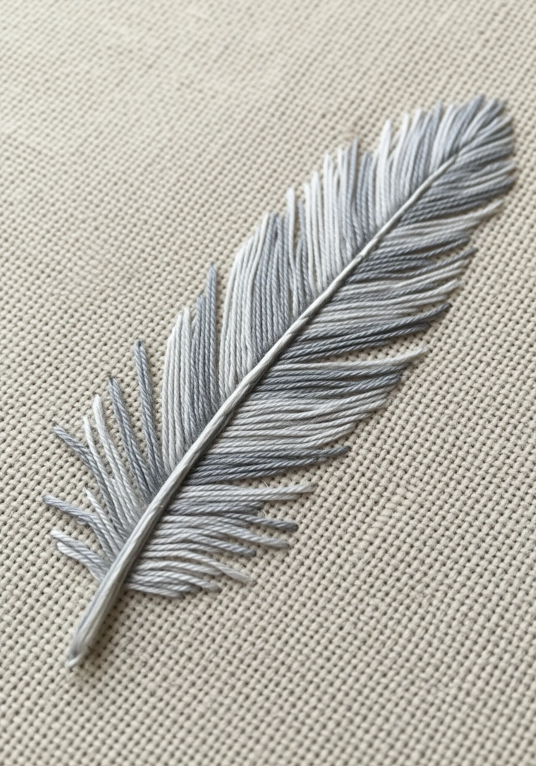 A realistic feather embroidered with blended shades of gray and white thread.
