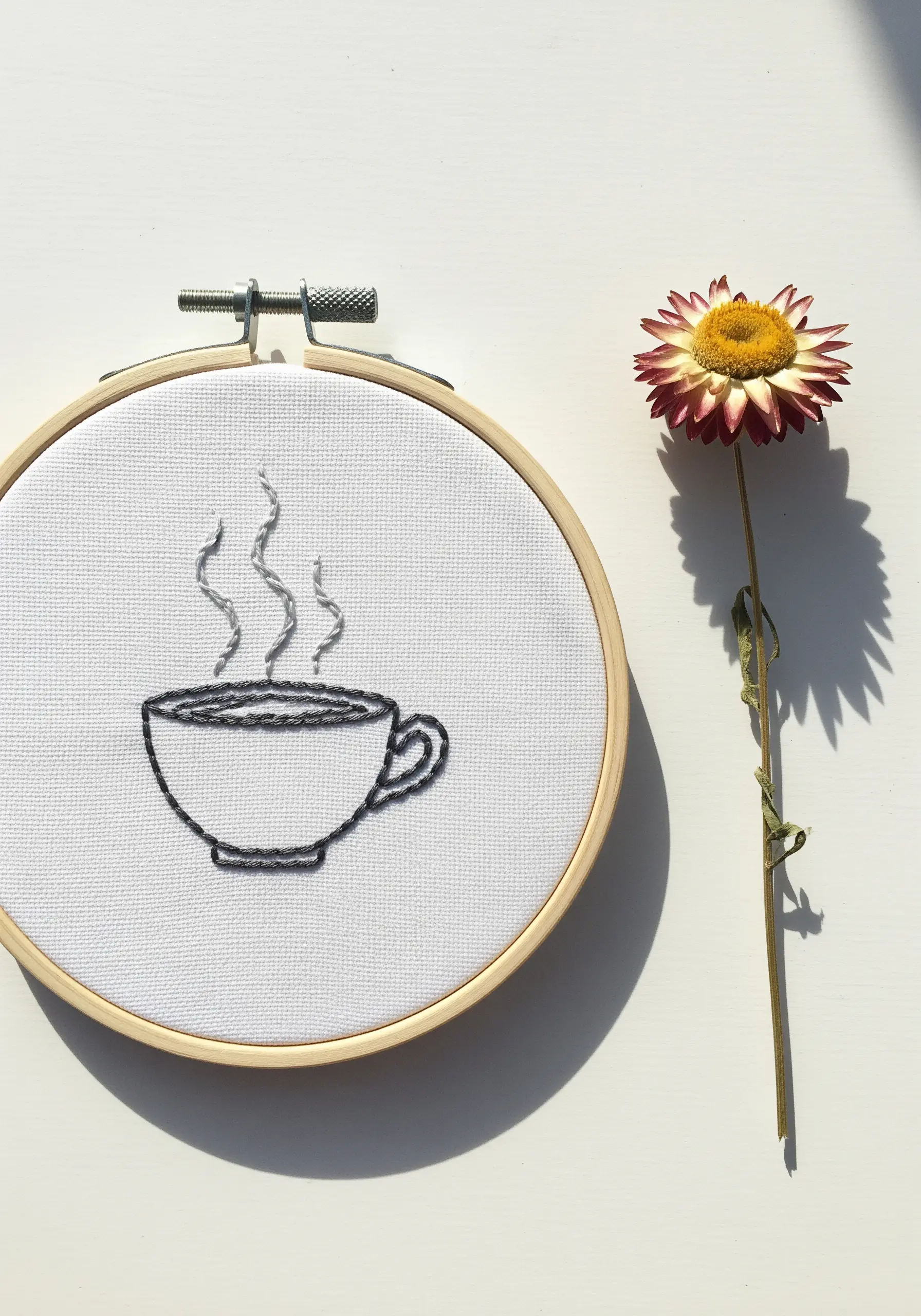 Line art embroidery of a steaming coffee cup in a wooden hoop.