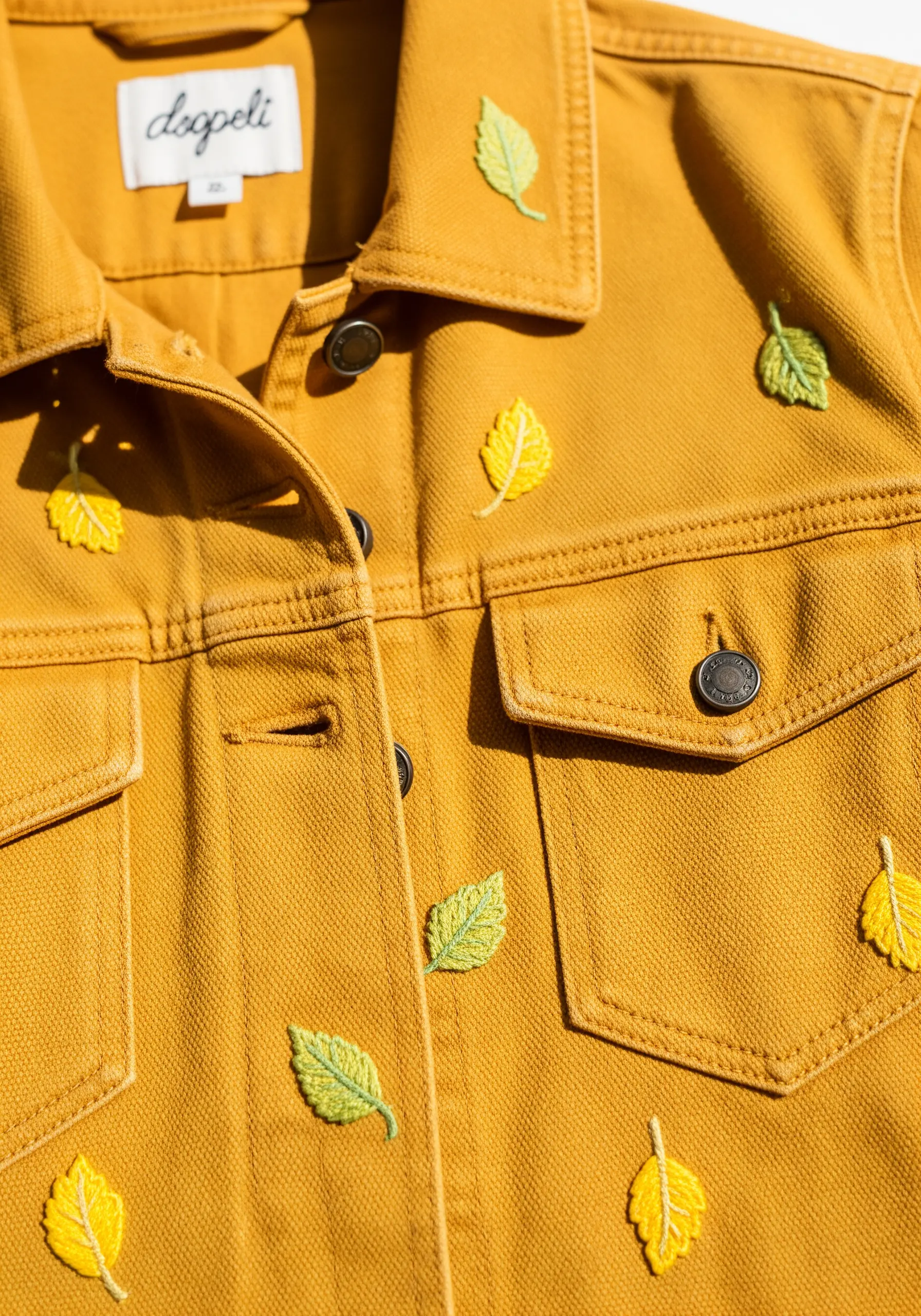 Tiny scattered leaves embroidered in two-tone yellow and green on a mustard jacket.