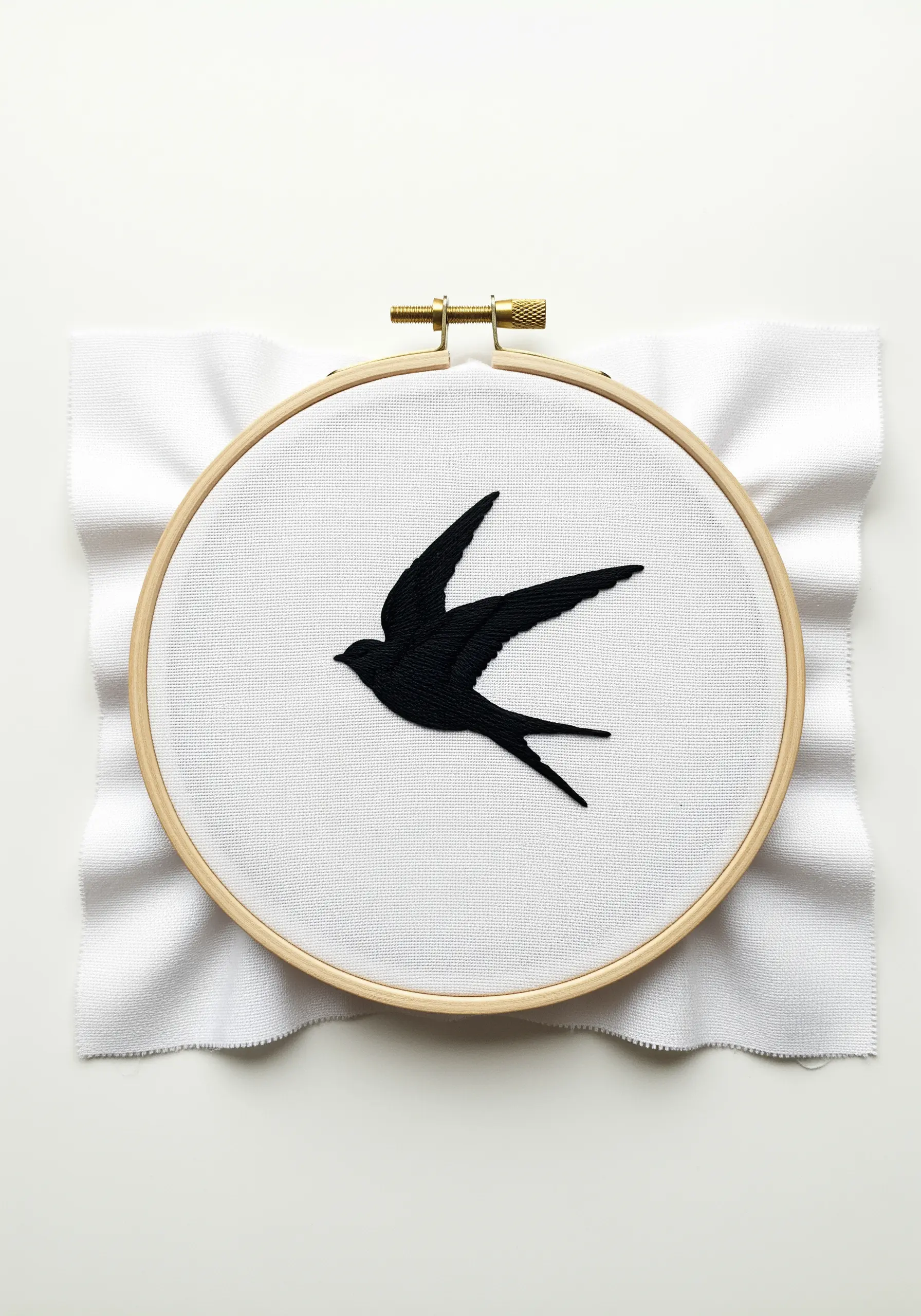 A solid black embroidered silhouette of a swallow in flight on white fabric.