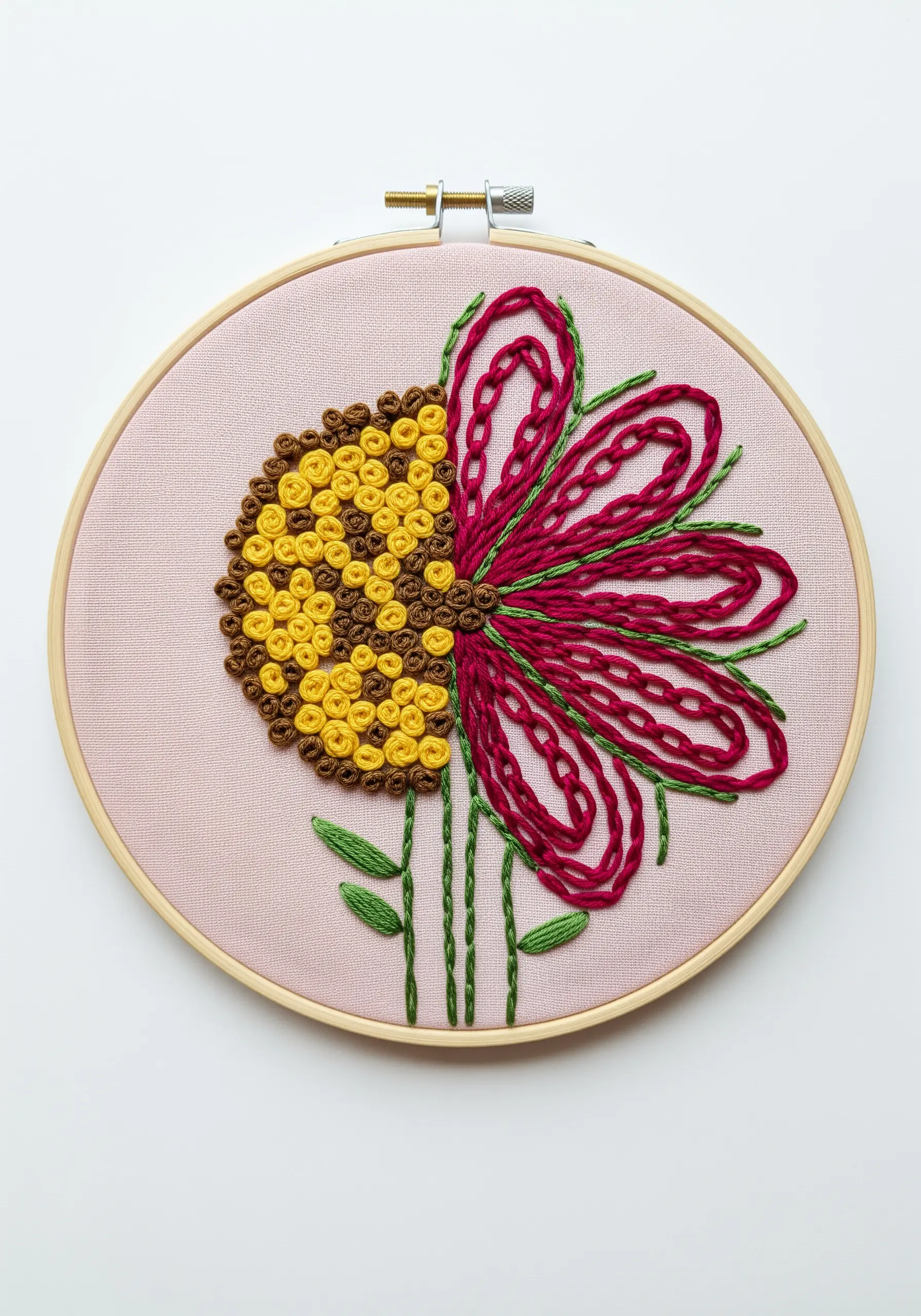 A flower embroidered in two halves, one with yellow French knots, the other with pink chain stitch.