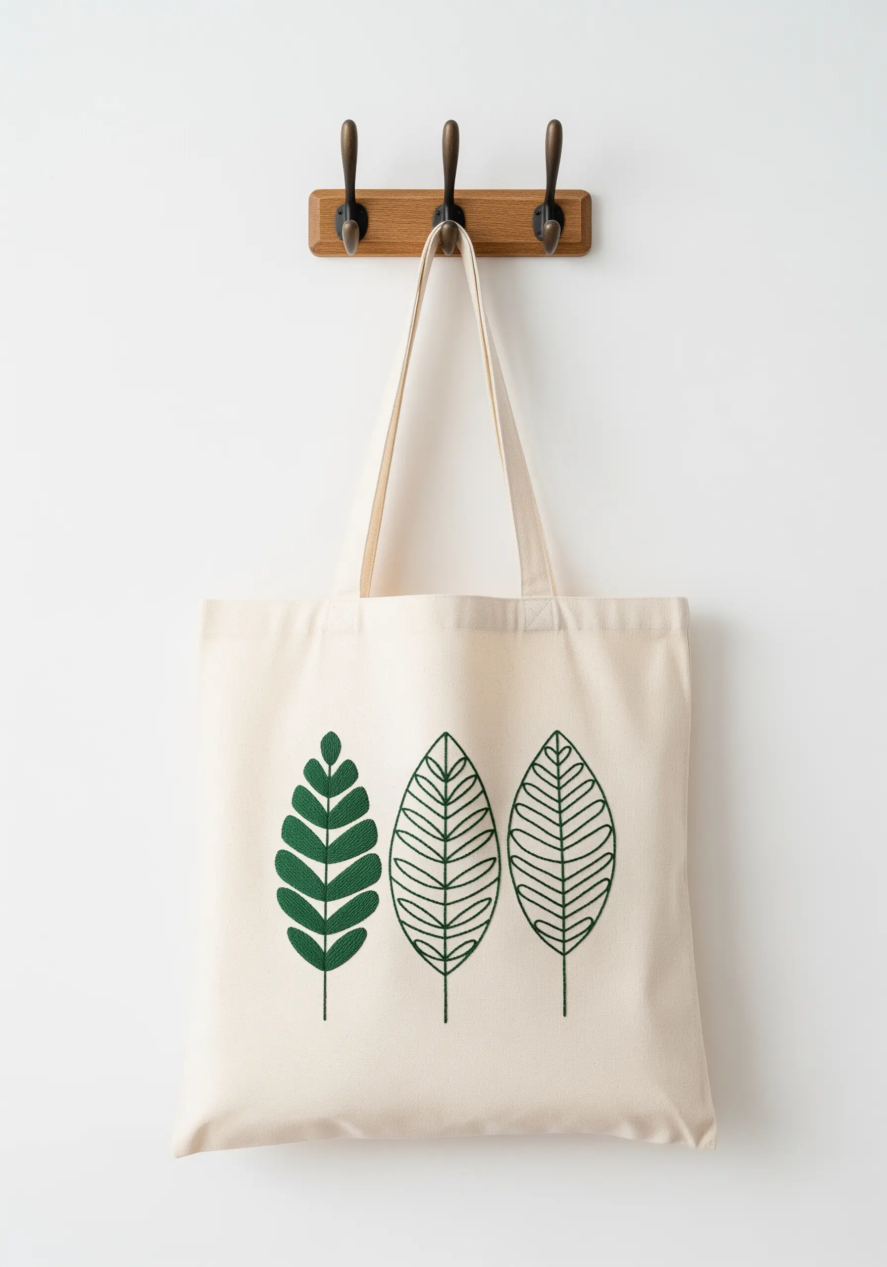 Three embroidered green leaf motifs on a canvas tote bag, each with a different stitch fill.