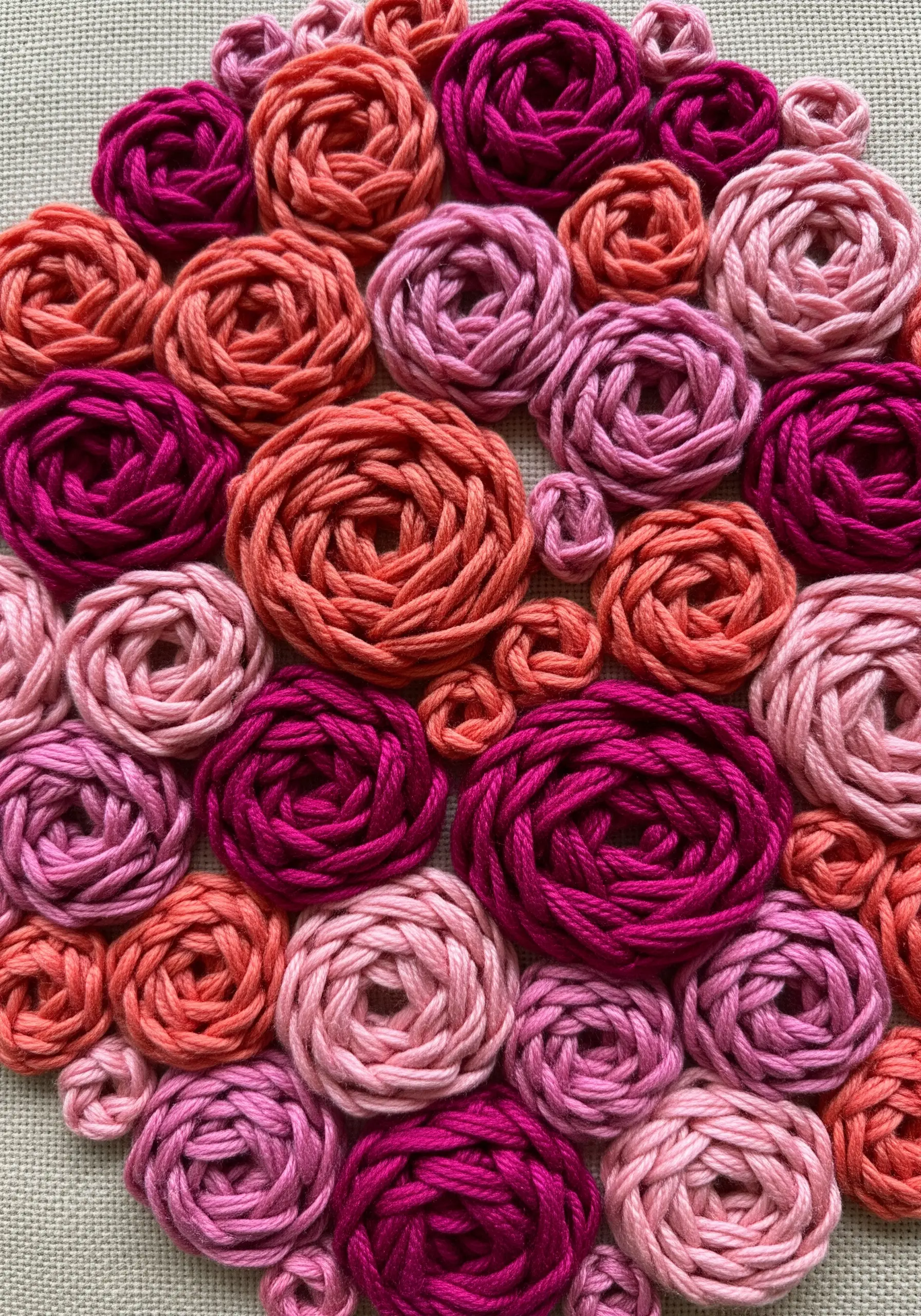 A dense cluster of woven wheel roses in shades of pink, coral, and magenta fills the frame.