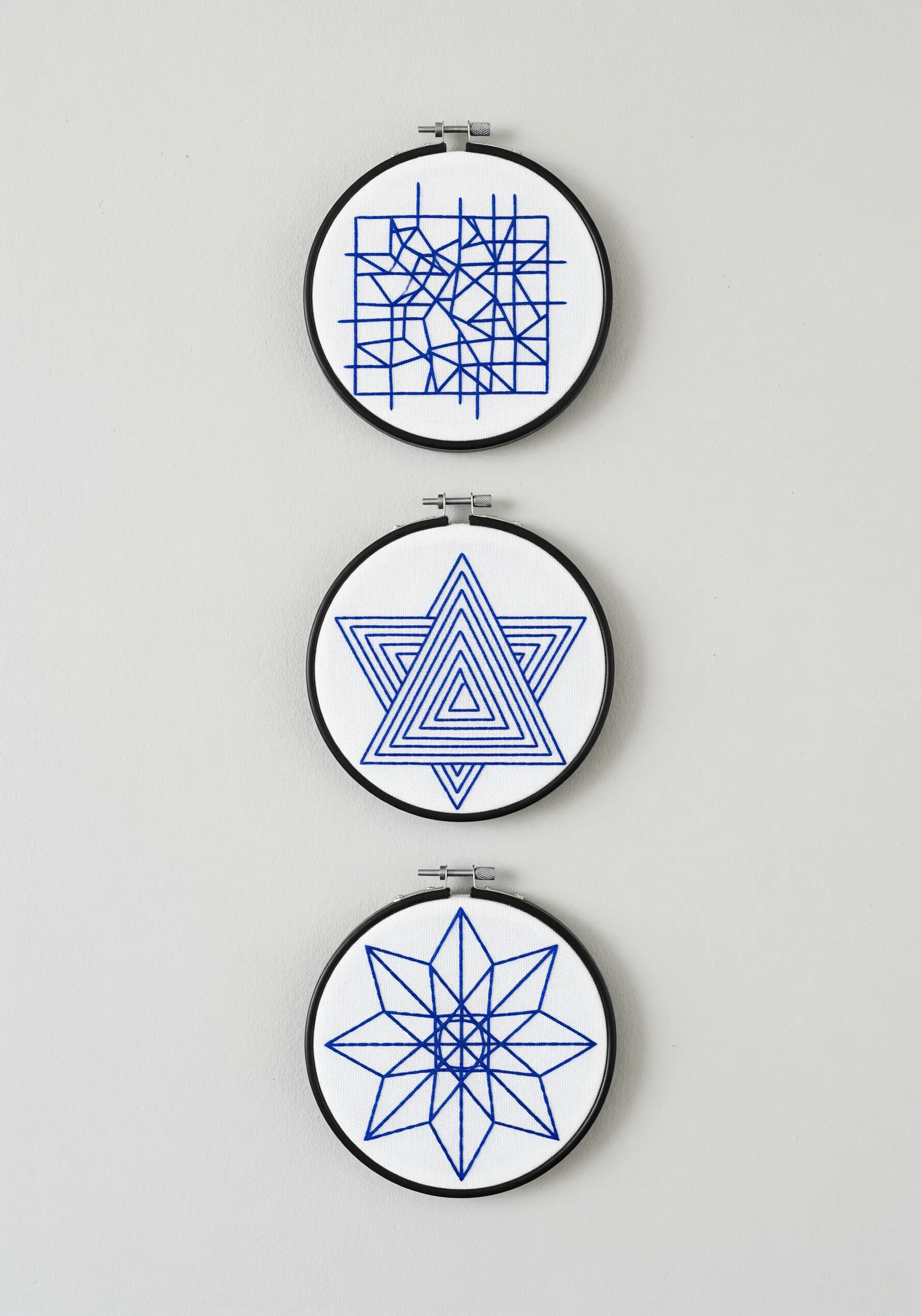 A set of three small embroidery hoops with precise blue geometric line-art patterns.