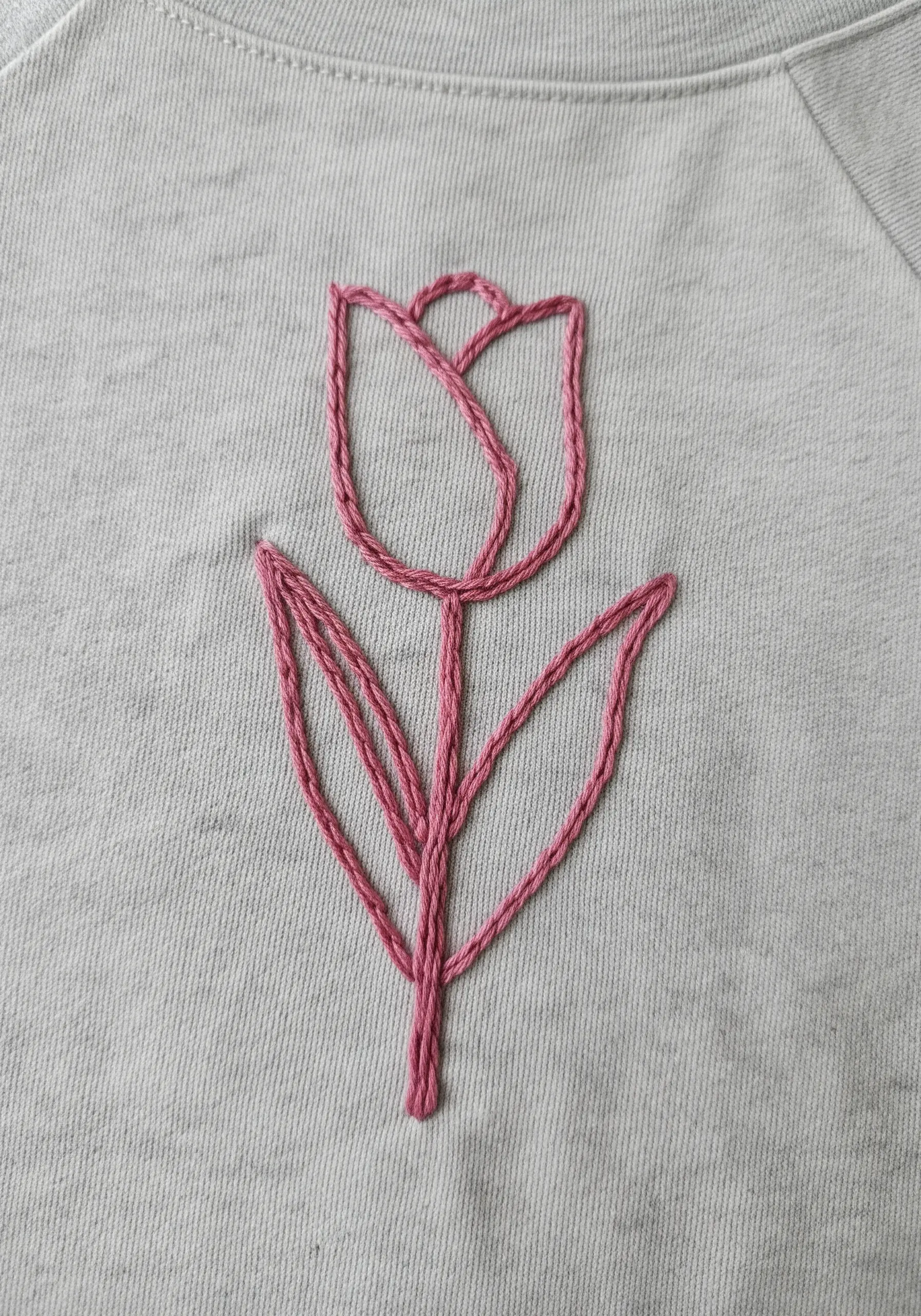 A simple pink outline of a tulip flower embroidered on a gray sweatshirt.