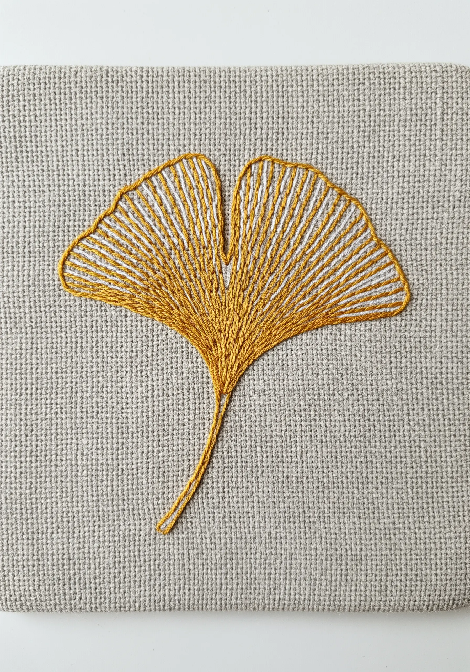 A ginkgo leaf embroidered with alternating yellow and white vertical stitches.