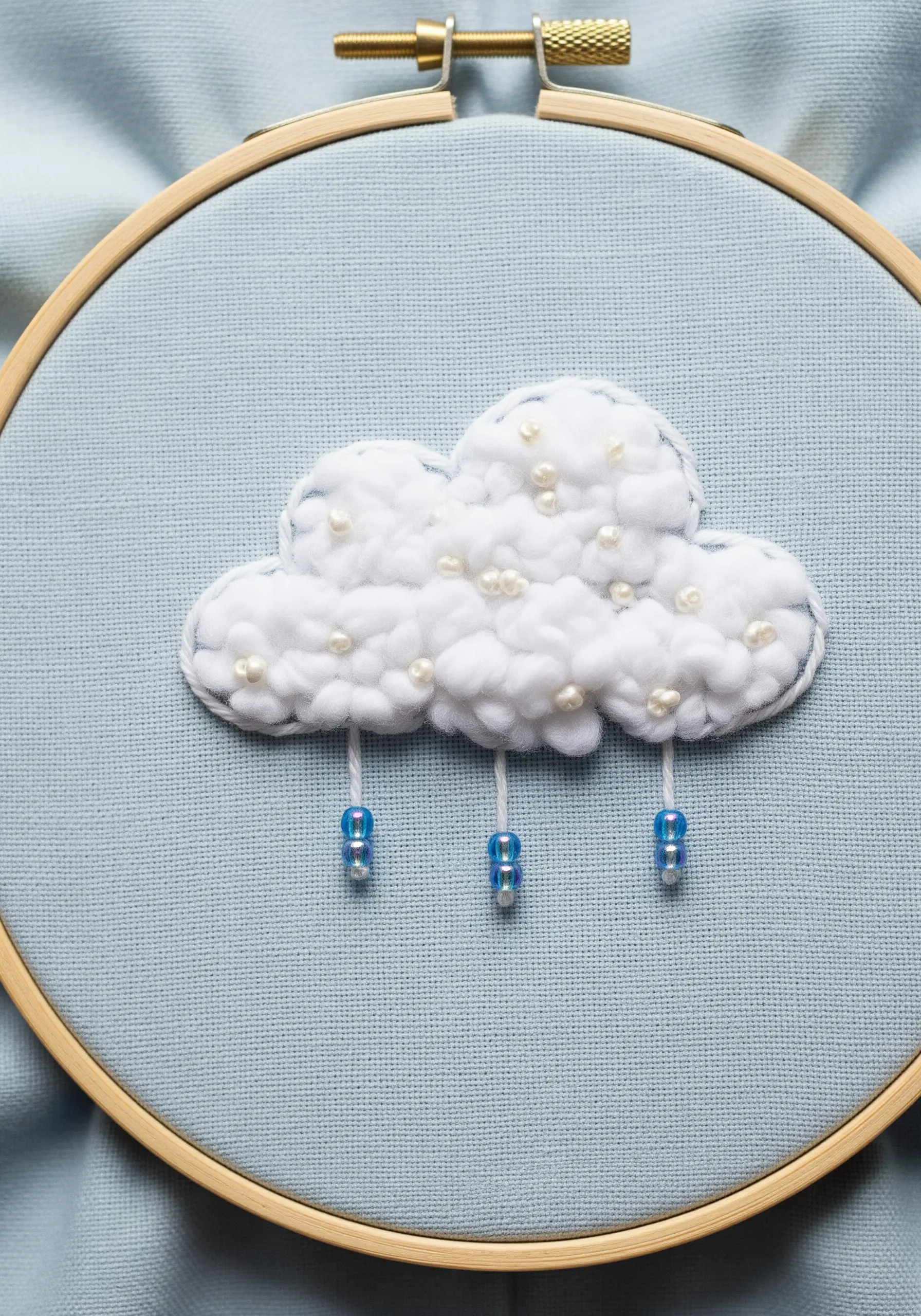 A fluffy embroidered cloud made with French knots and pearls, with beaded raindrops.