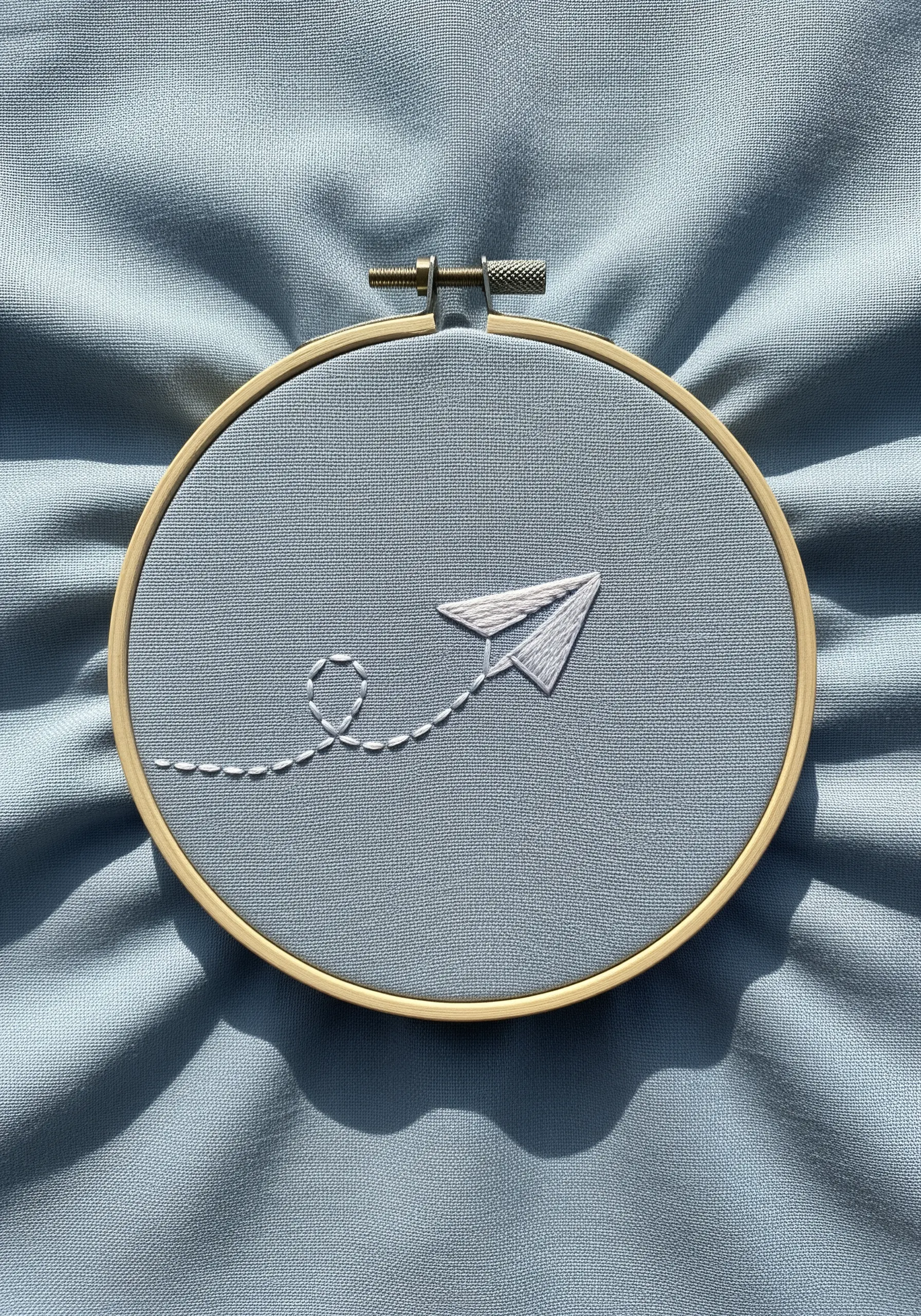 A simple paper airplane with a looped, dashed flight path on blue fabric.
