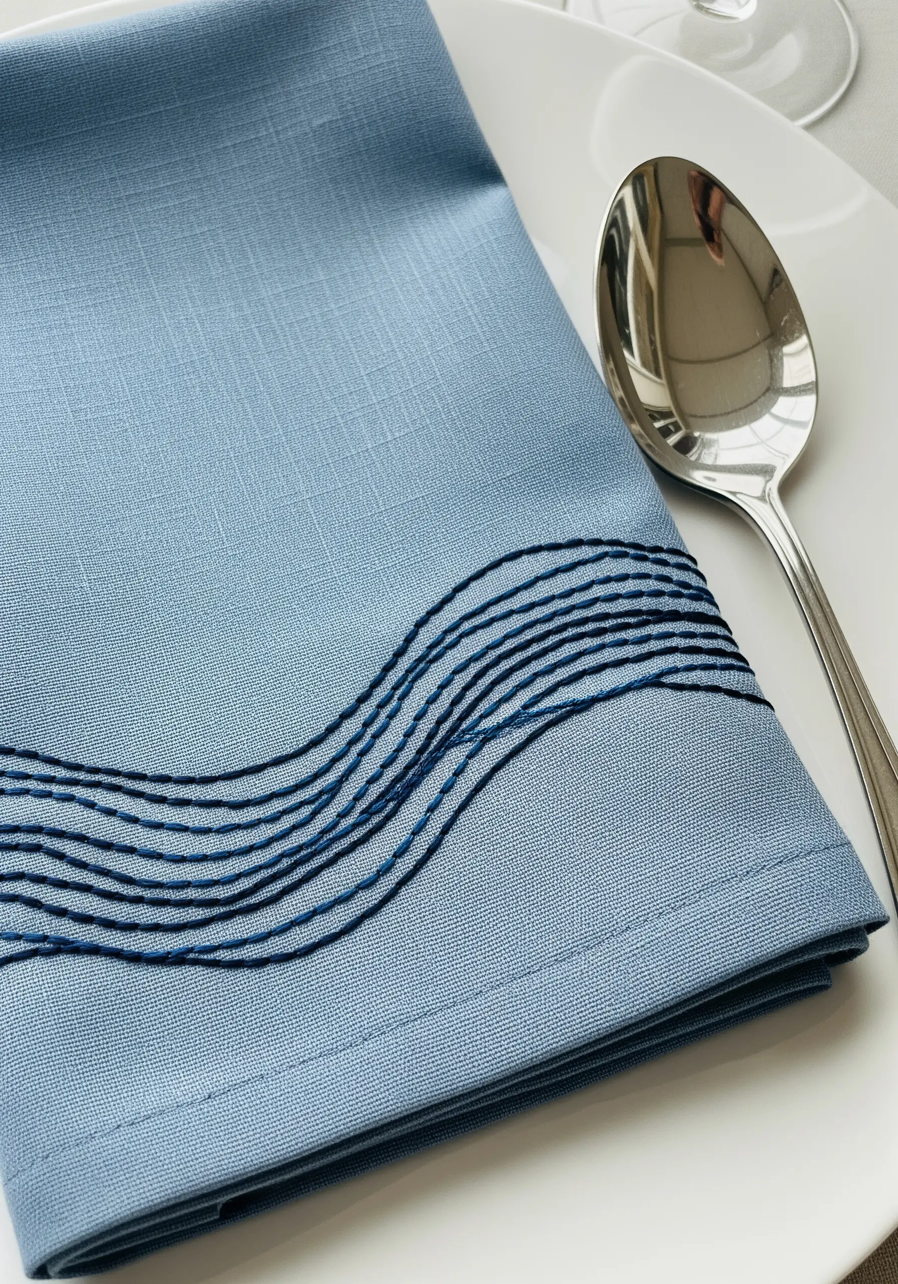 Abstract wavy lines in shades of blue embroidered on a dusty blue napkin.