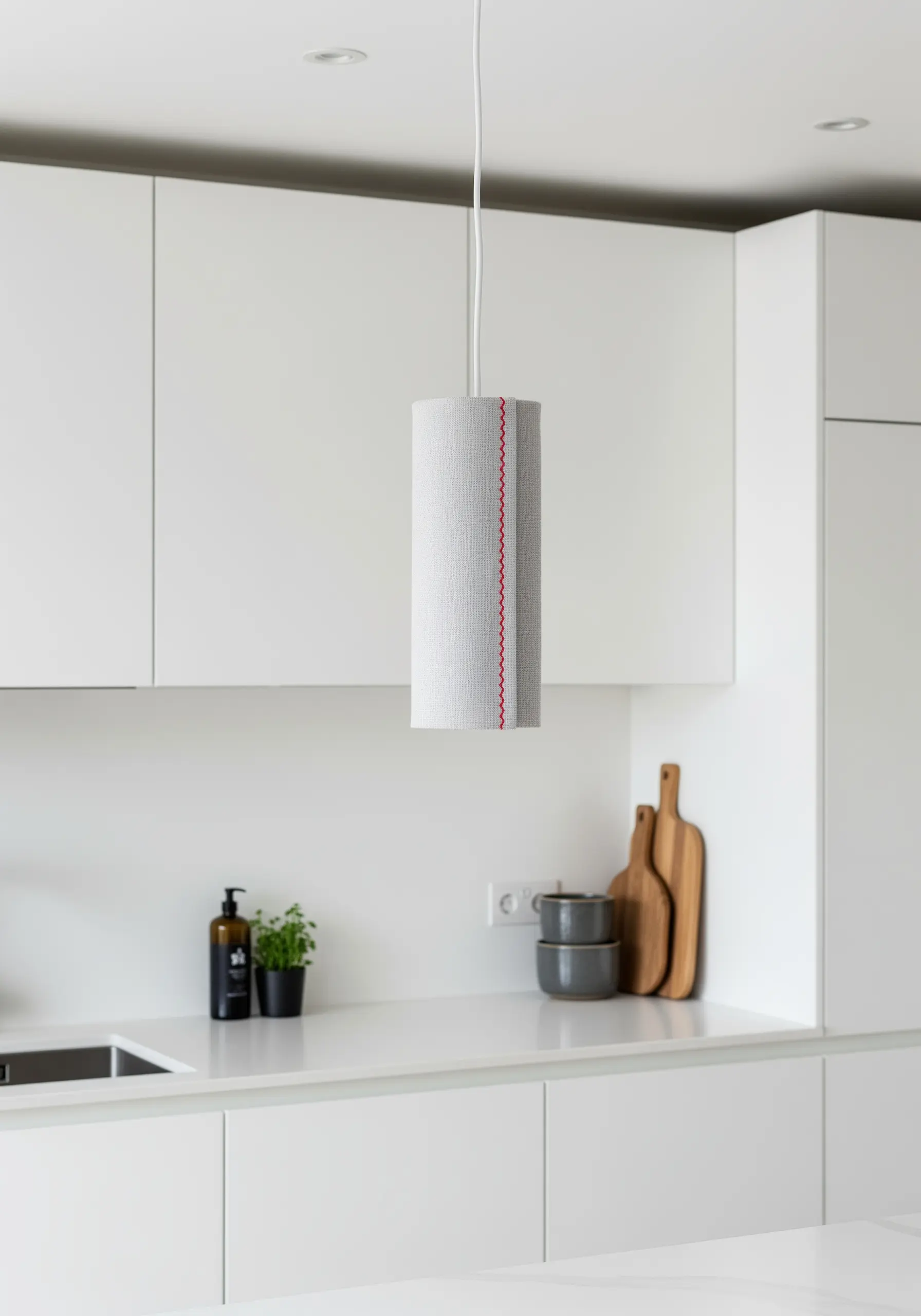 A grey cylindrical pendant light with a single vertical line of red running stitches.