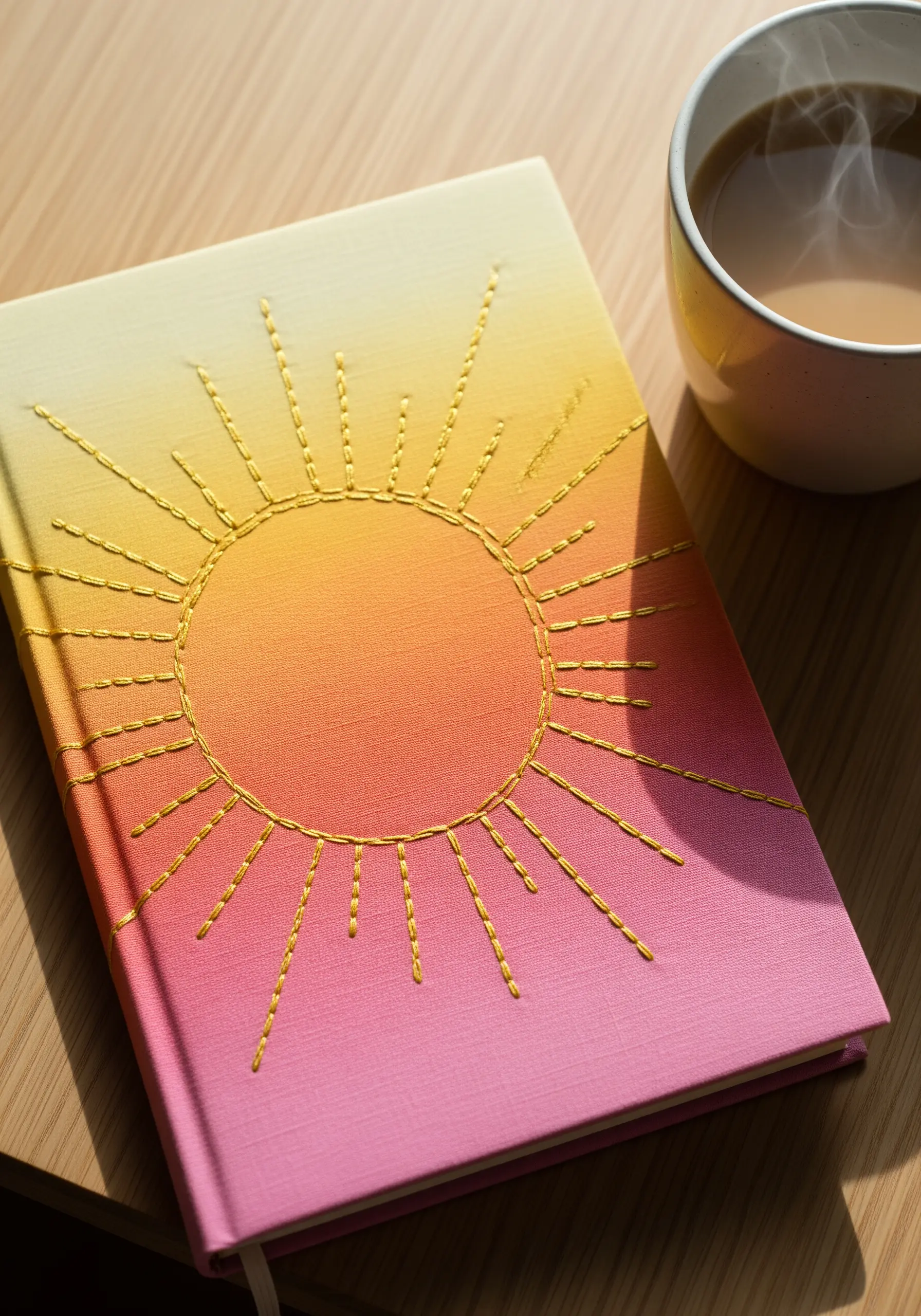 A sunburst pattern stitched in gold thread on a pink, orange, and yellow gradient journal cover.