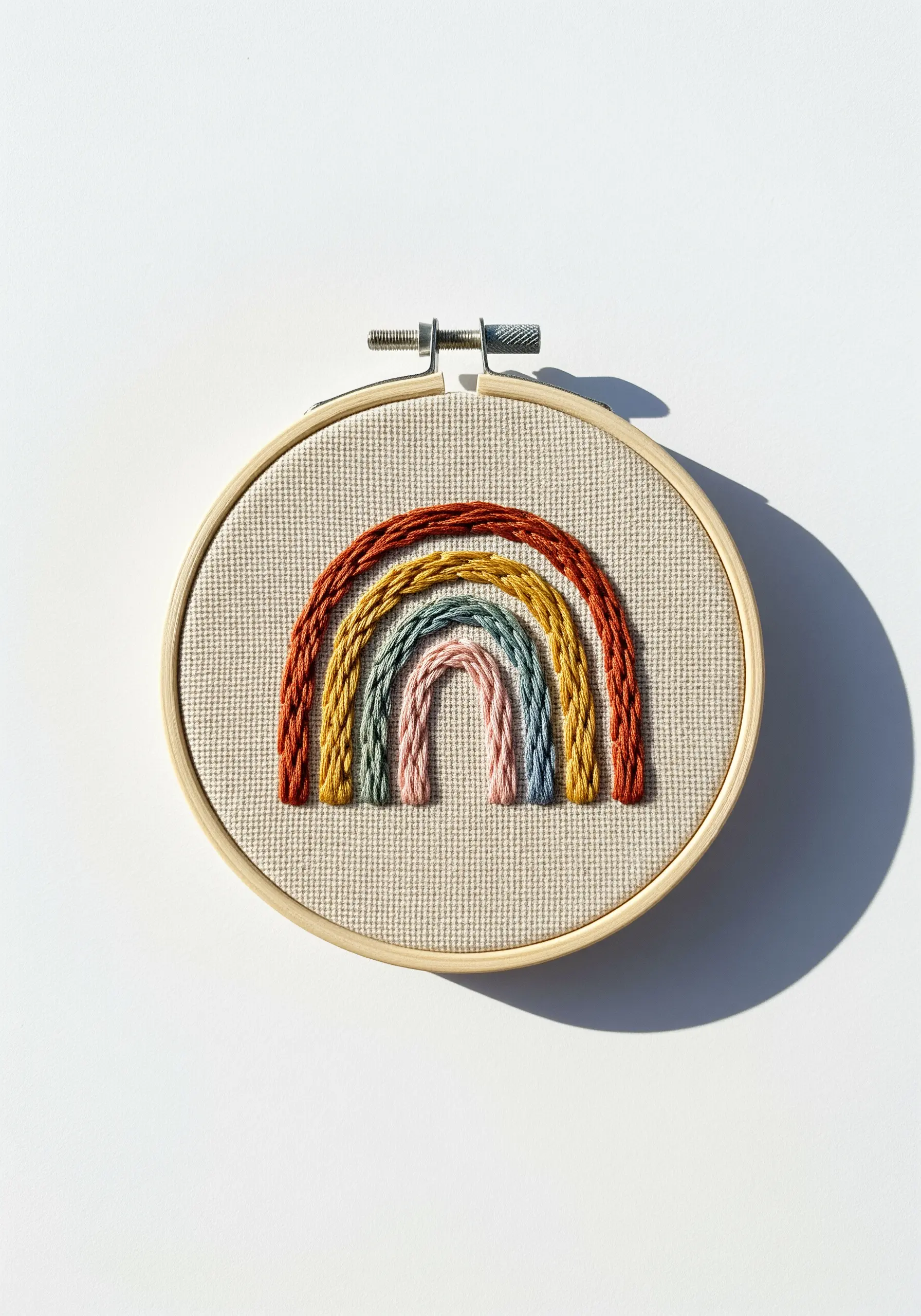 A boho rainbow with textured arcs made from chain stitches in earthy tones.