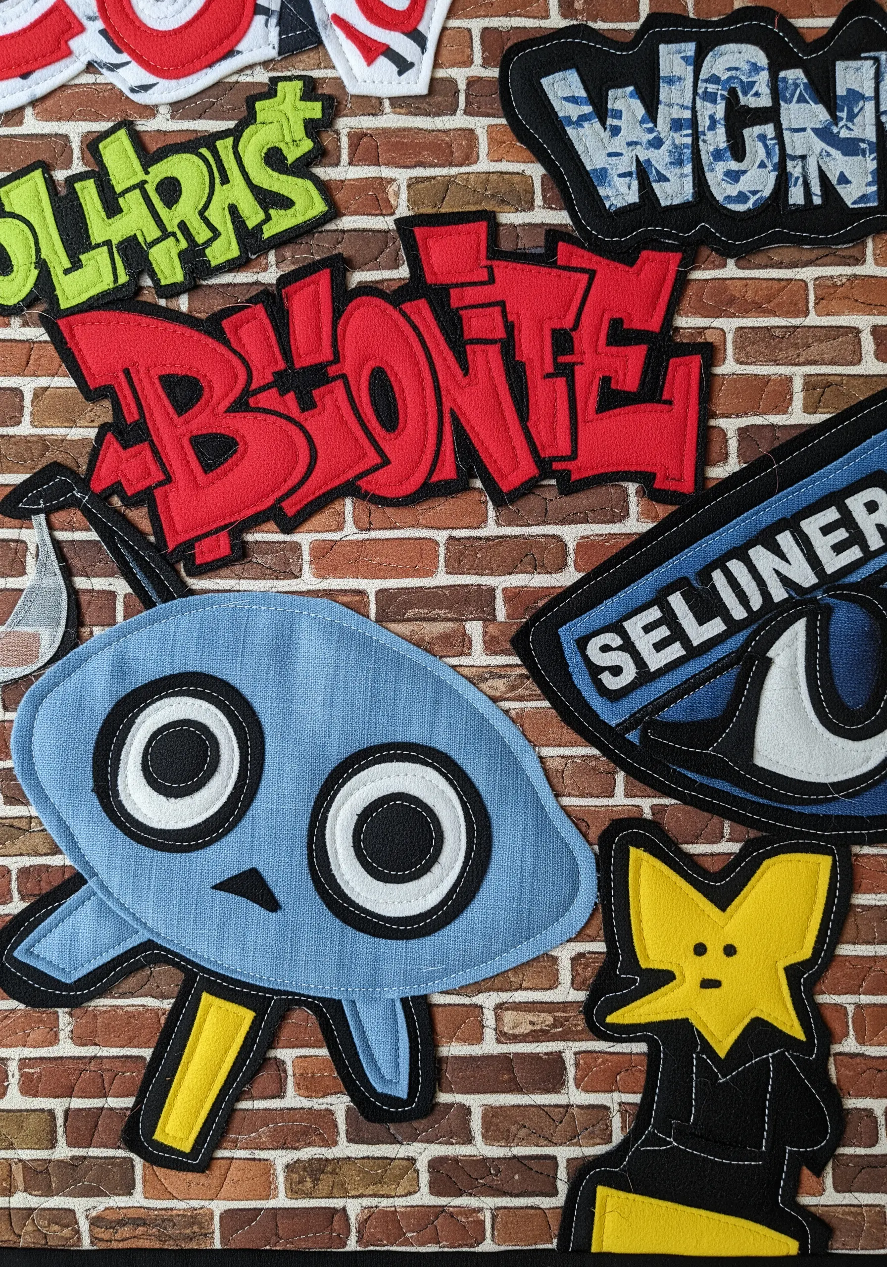 A quilted wall hanging with colorful, graffiti-style appliqué letters and characters.