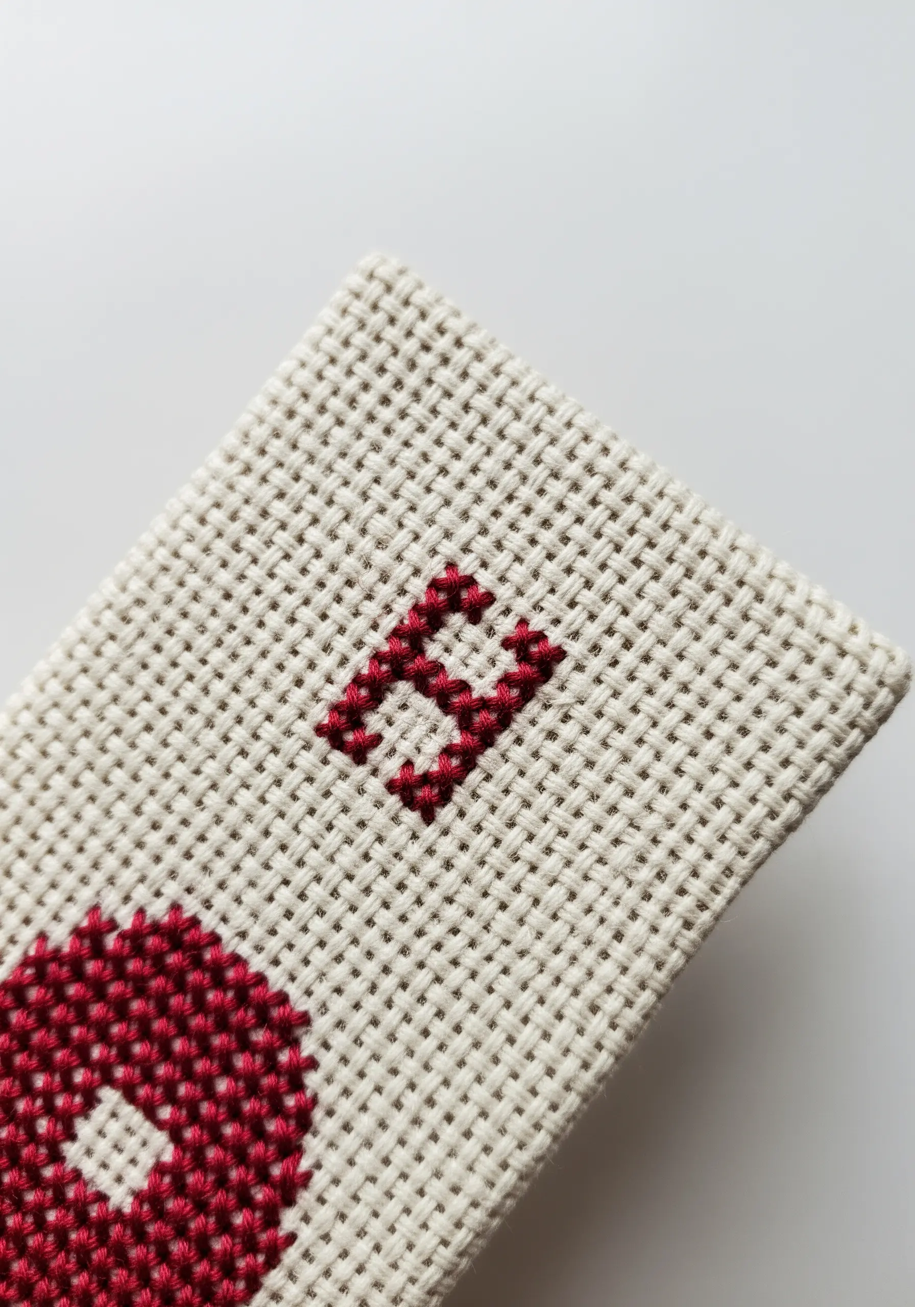 A crisp, red cross-stitched monogram on a structured, even-weave canvas.
