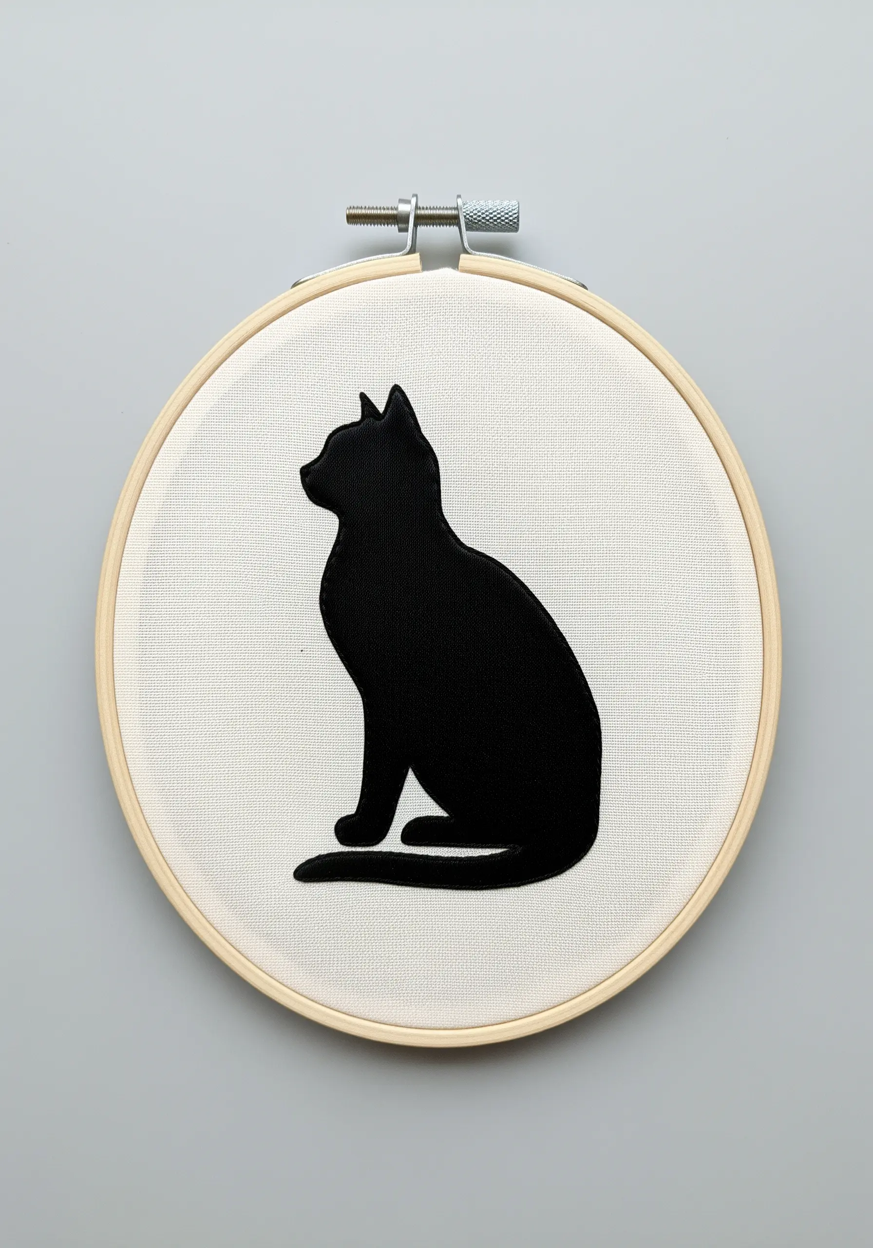 A solid black cat silhouette embroidered on off-white fabric in a hoop.