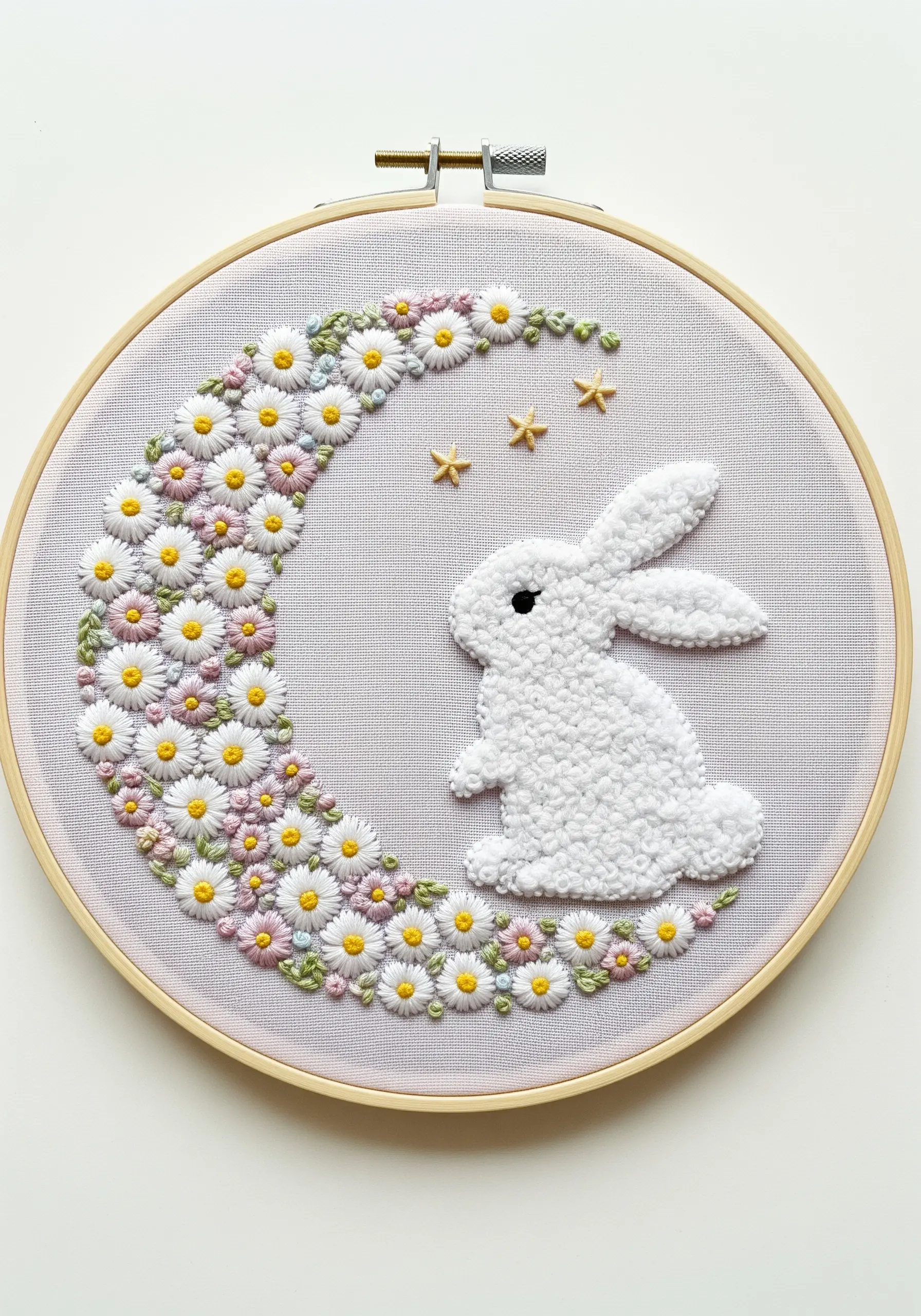 A fluffy white bunny made with turkey stitch next to a crescent moon of daisies.