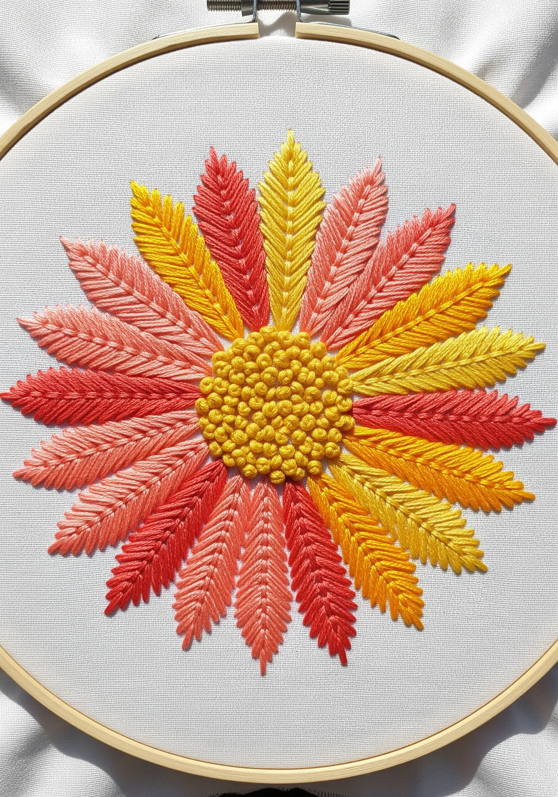 Floral mandala with gradient petals in pink, yellow, and red, with a French knot center.