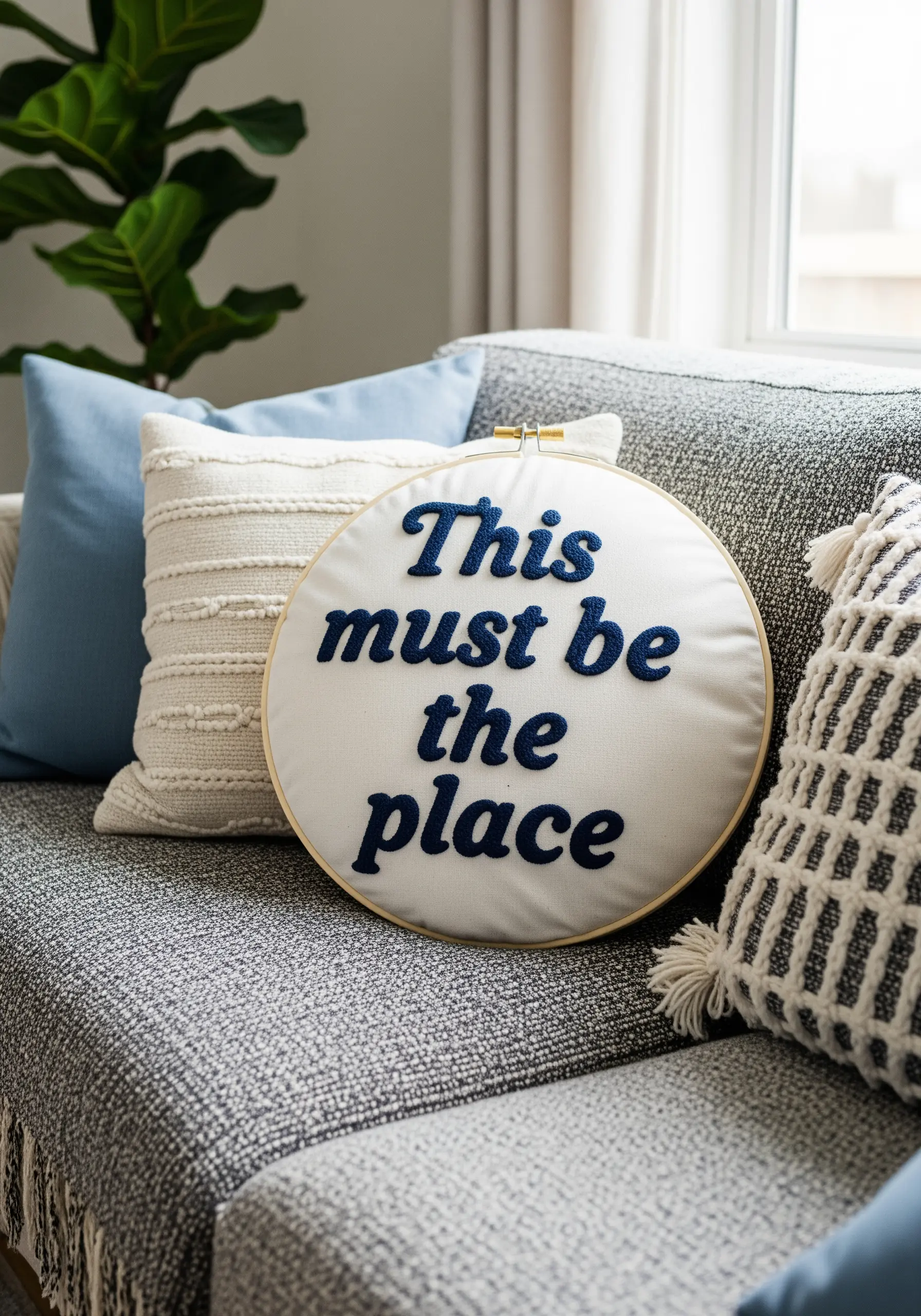 A quote with bold, navy blue appliqué letters on a soft white fabric cushion.