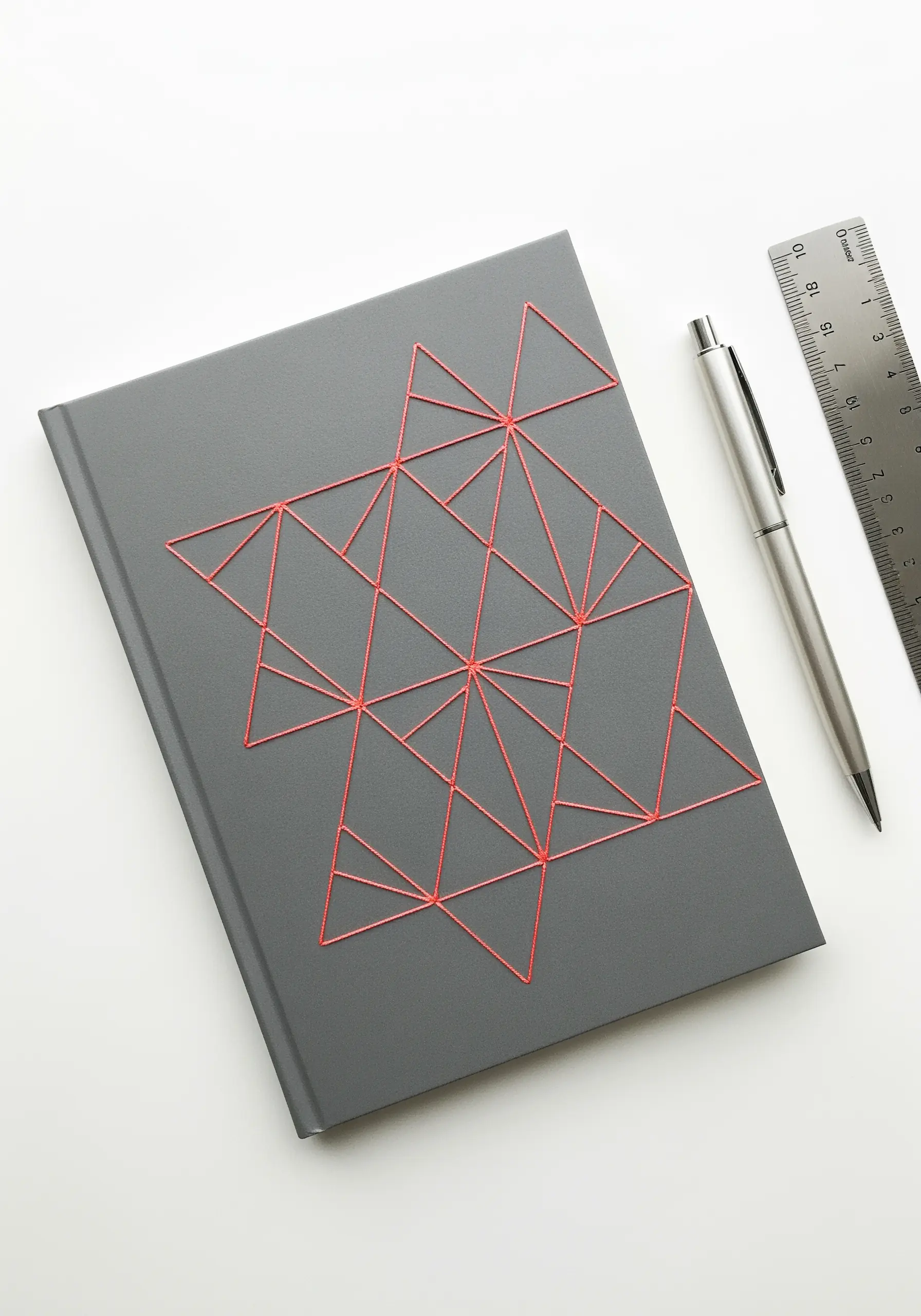 A gray hardcover journal with a geometric pattern stitched in bright coral thread.