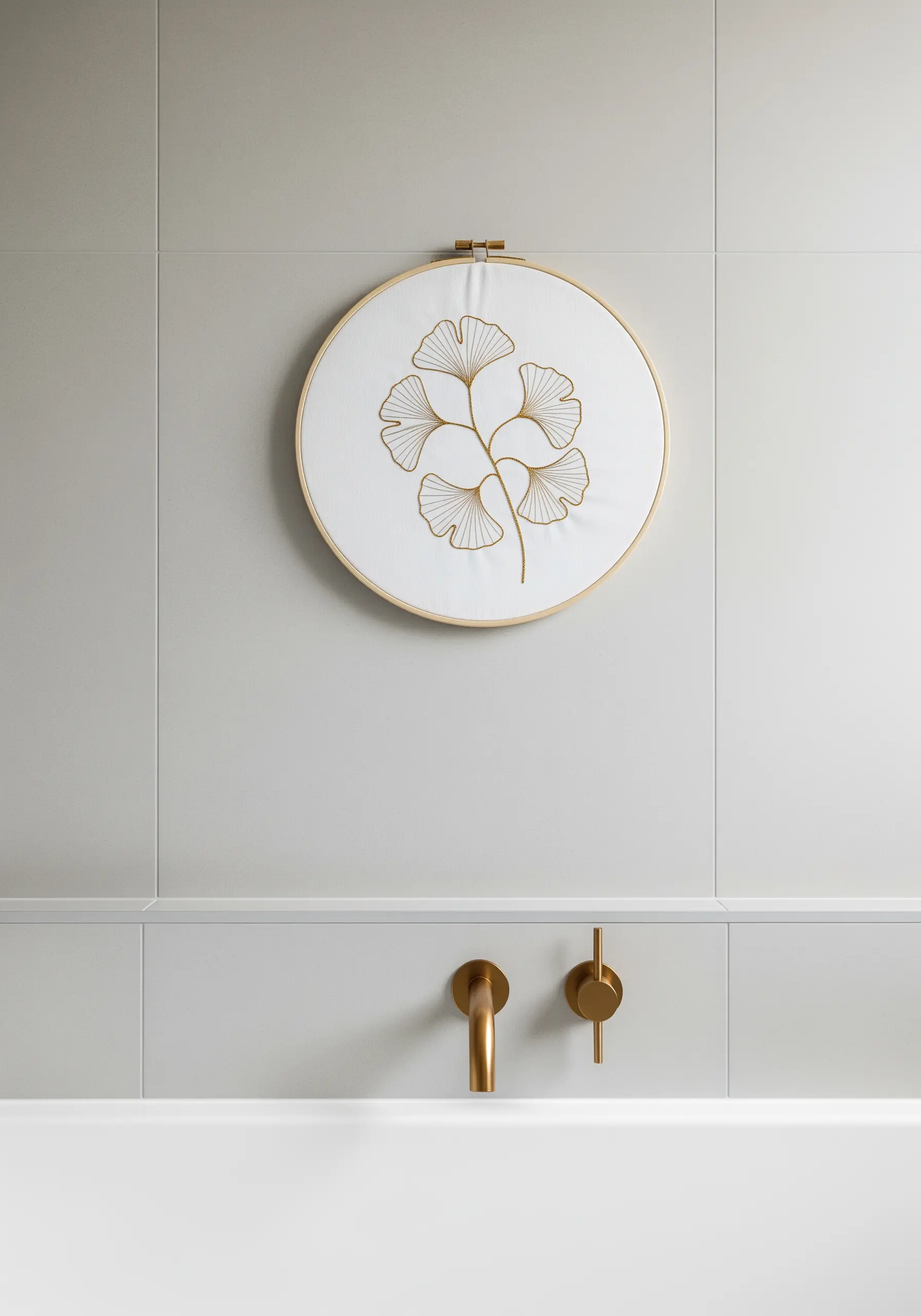 Minimalist gold thread embroidery of a ginkgo branch on white fabric in a hoop.