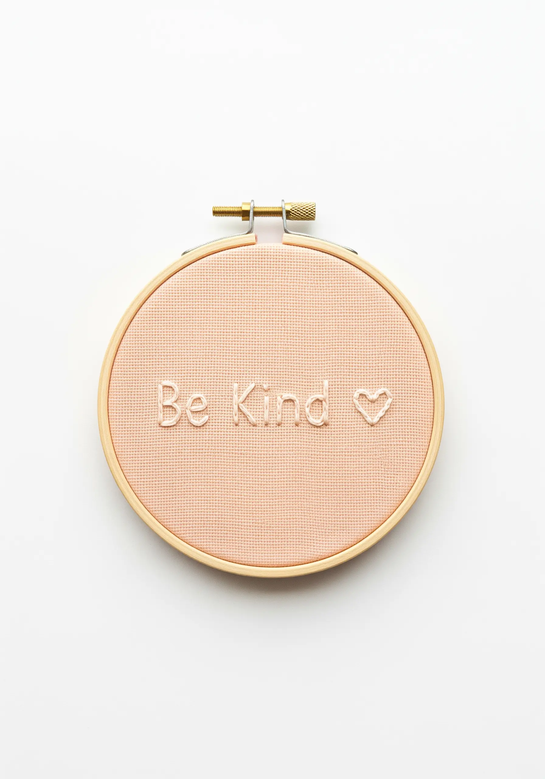 'Be Kind' and a heart outline embroidered in light thread on pale pink fabric.