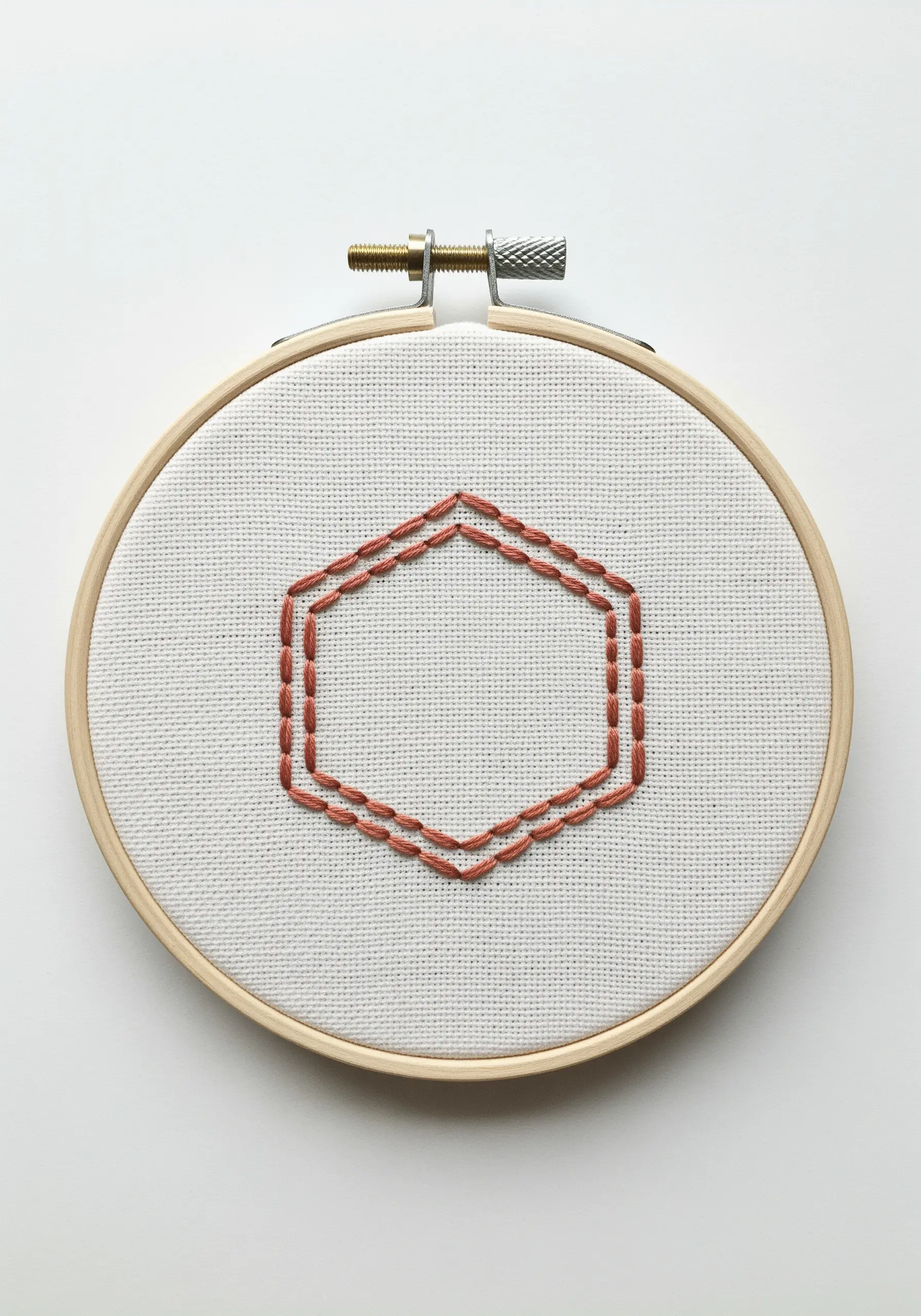 A geometric hexagon outline embroidered in a double line of running stitch.