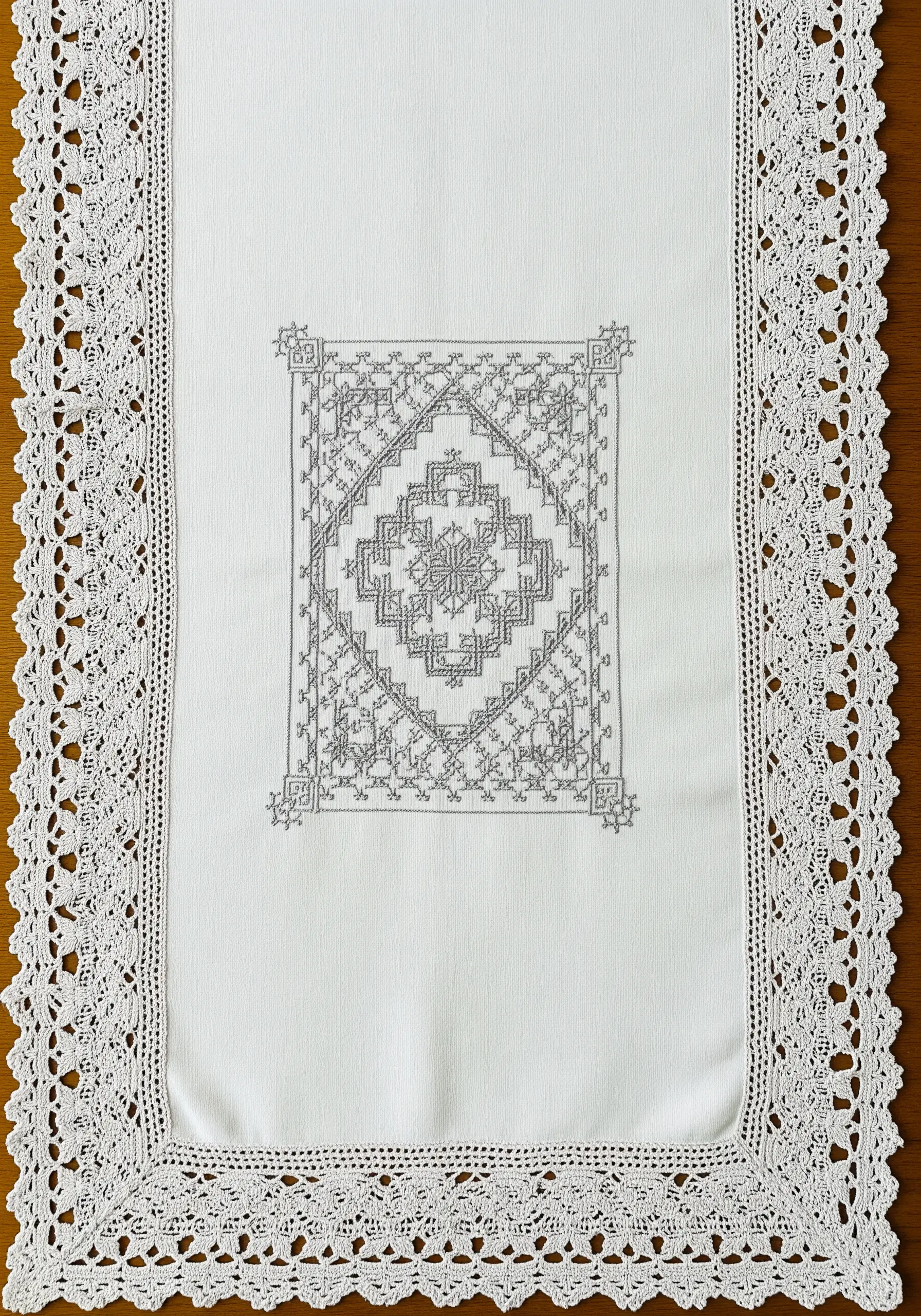 Geometric counted-thread embroidery pattern in grey on a white linen table runner.