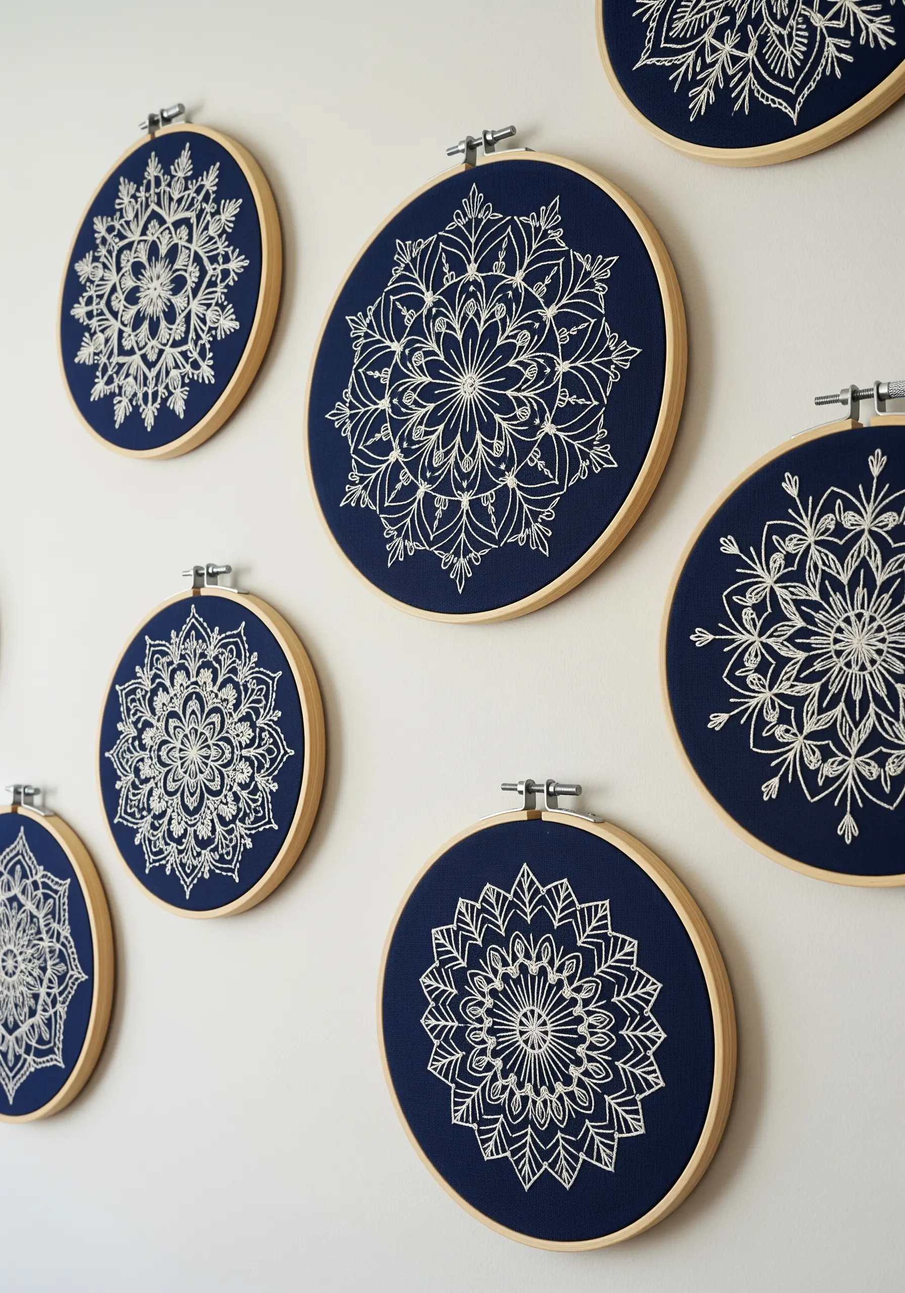 A collection of embroidery hoops with intricate white mandalas stitched on navy blue fabric.
