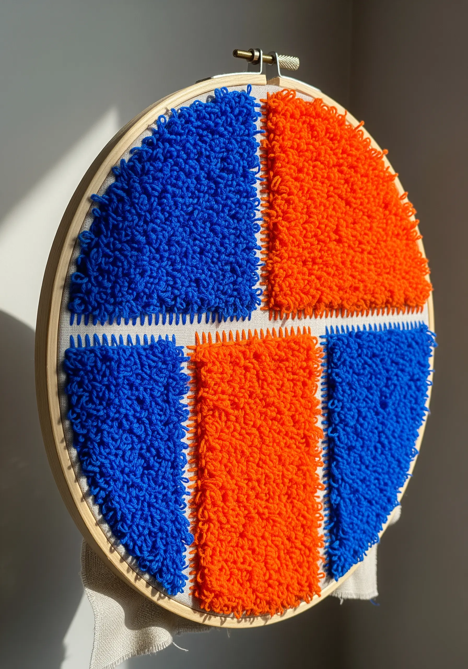 A color-blocked punch needle hoop with dense blue and orange yarn loops.