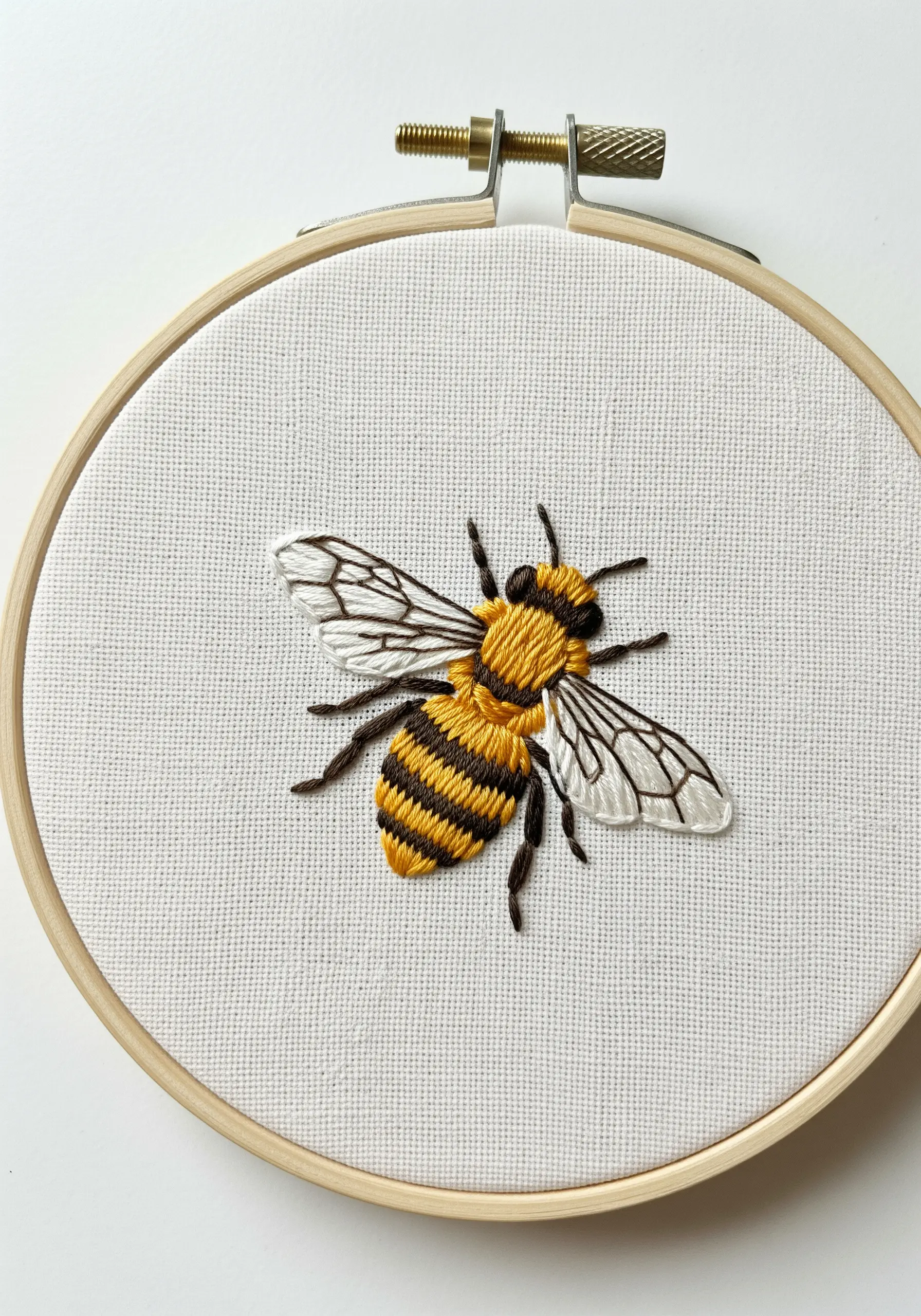 Realistic thread-painted bee with textured body and translucent wings on white fabric.