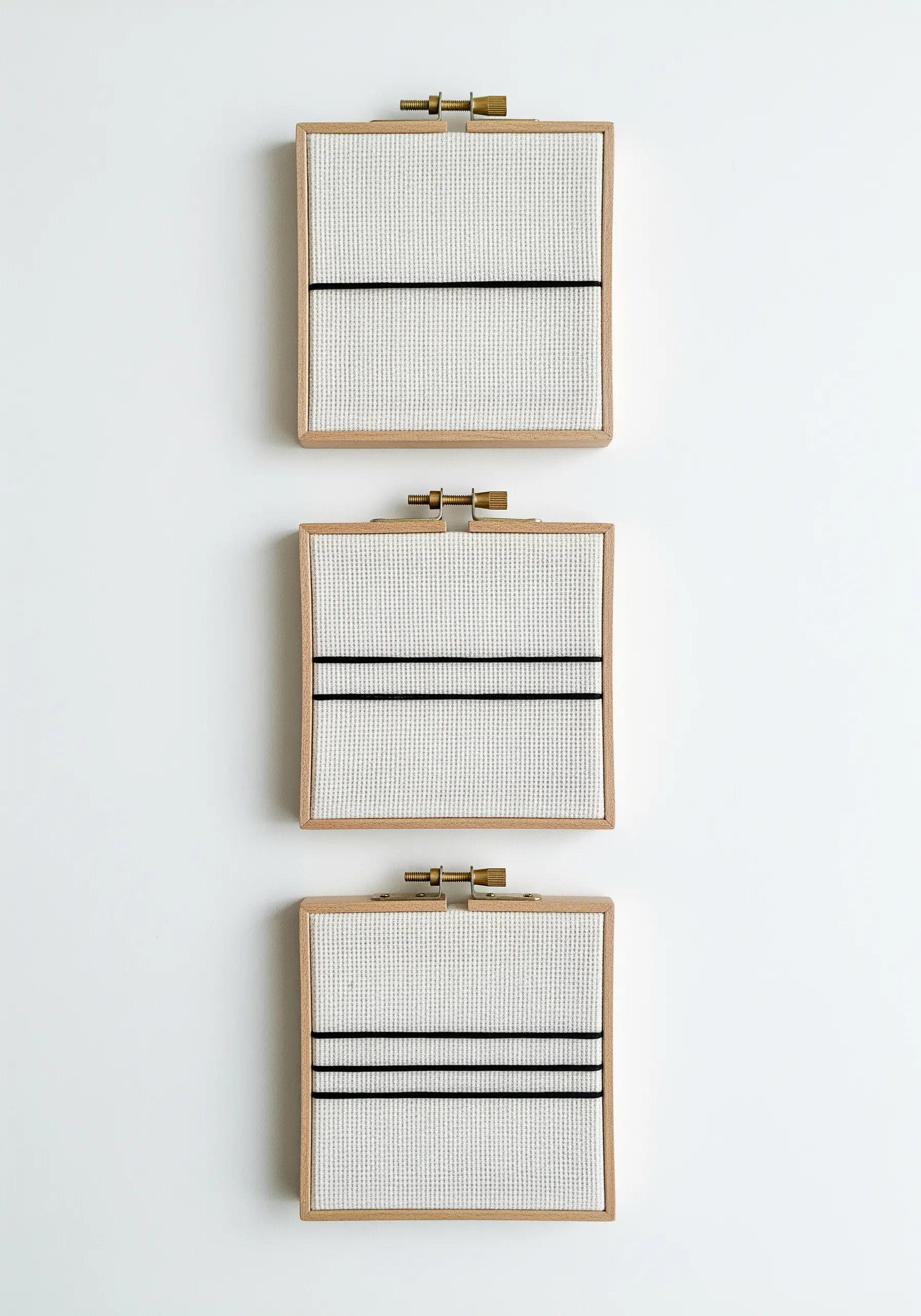 A triptych of three small rectangular hoops, each with a few minimal black horizontal lines.