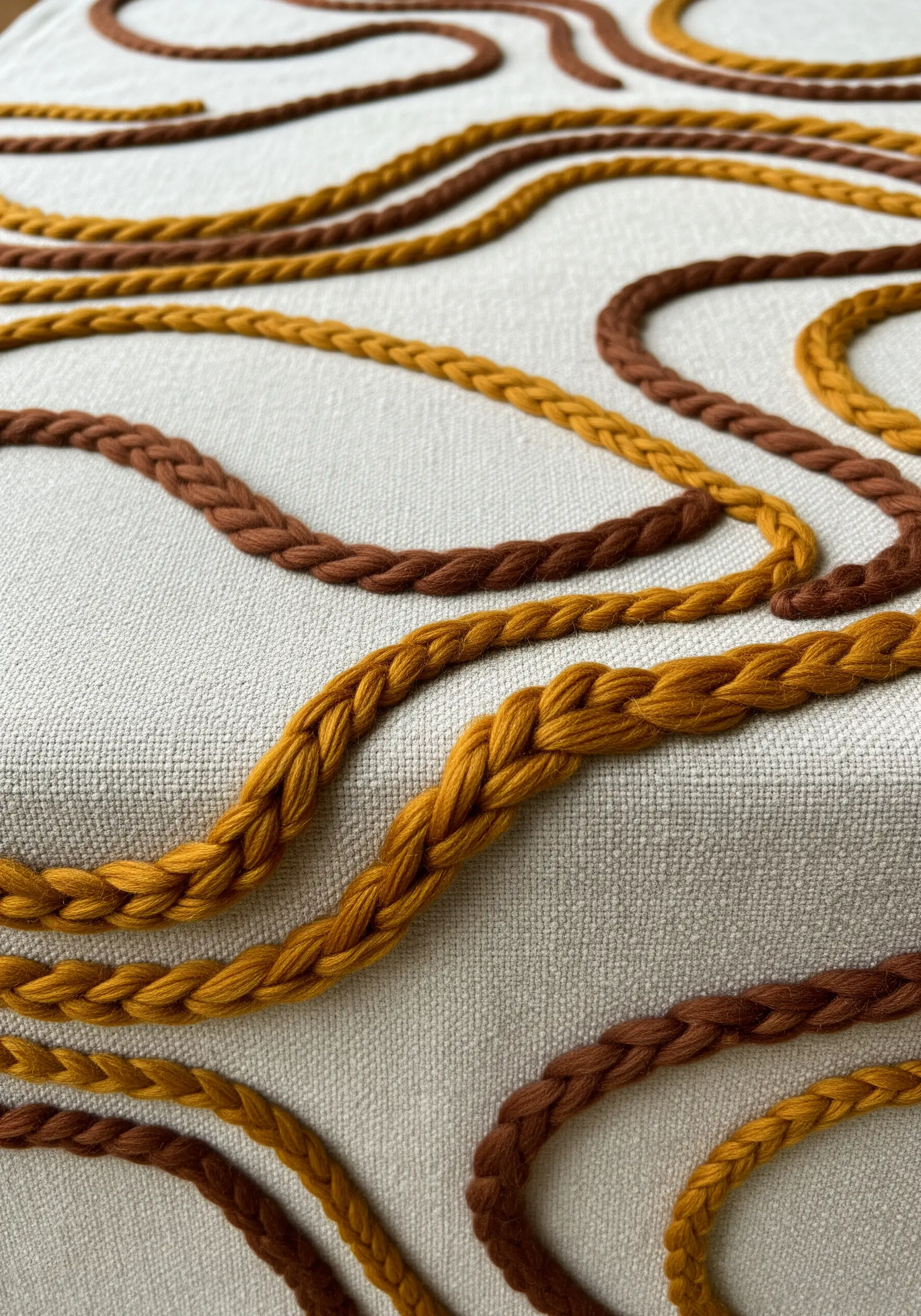 Thick, braided yarn in brown and gold stitched in wavy lines on a neutral tablecloth.