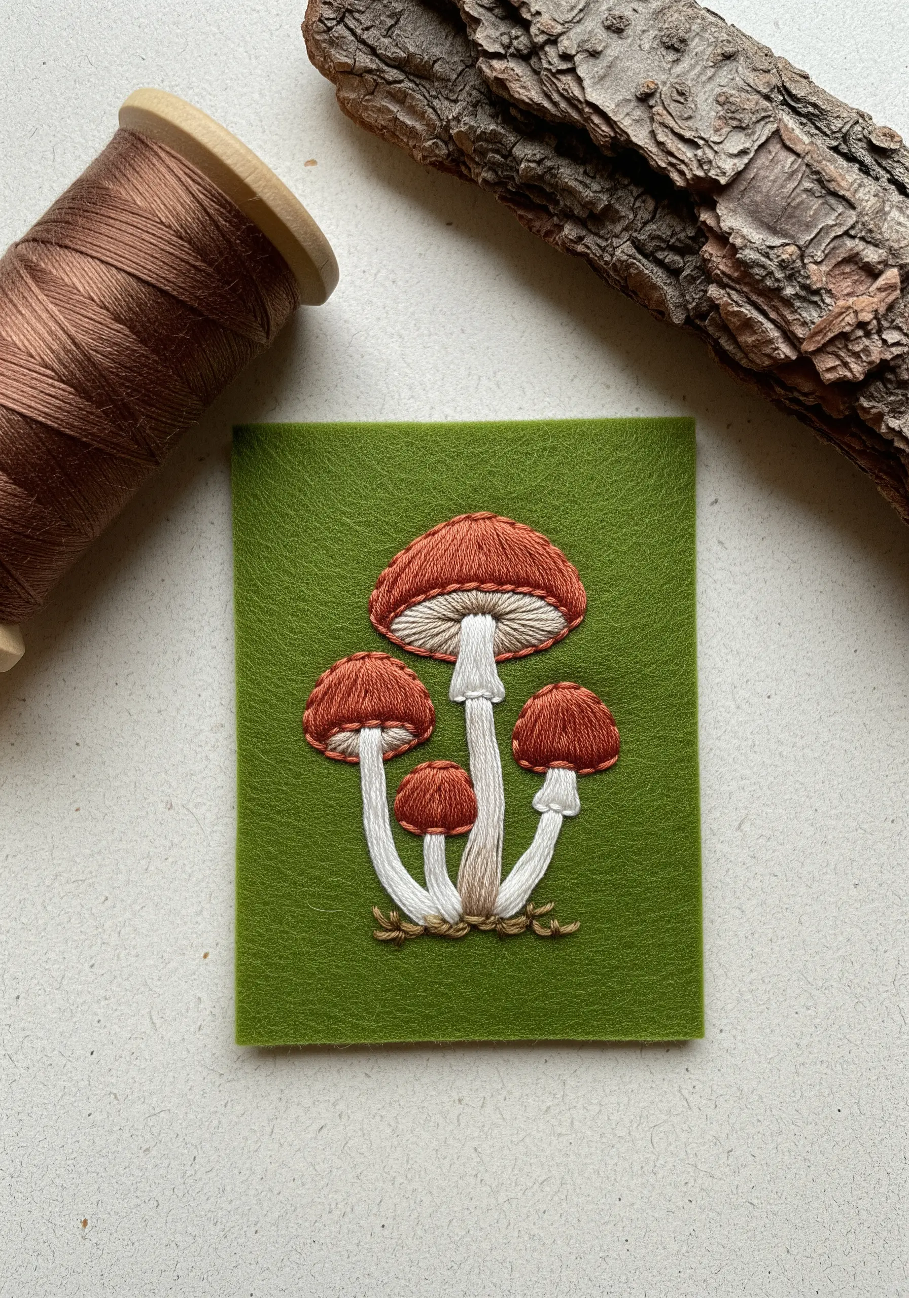 Detailed embroidery of mushrooms with color blending on a green felt background.