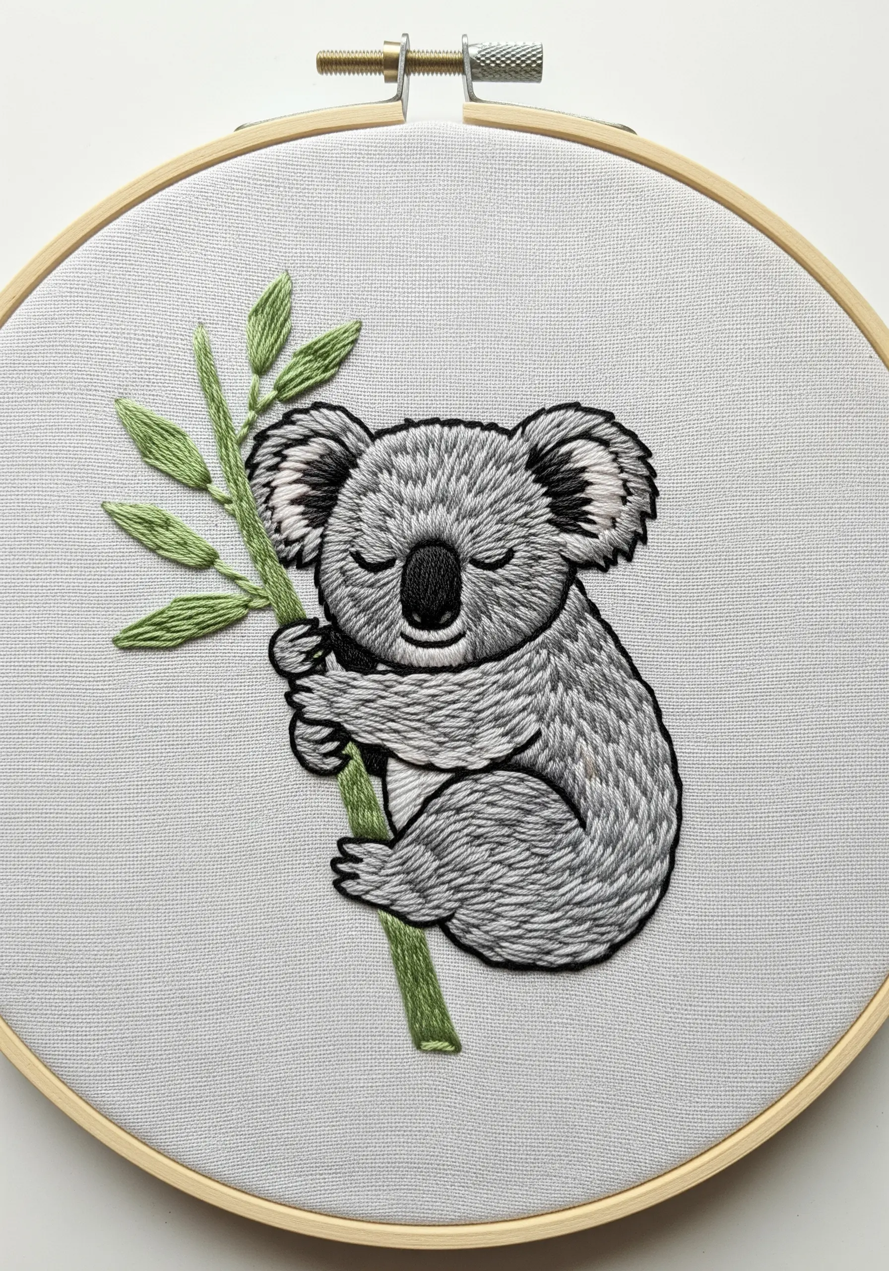 A sleeping koala on a branch, embroidered with blended shades of grey thread.