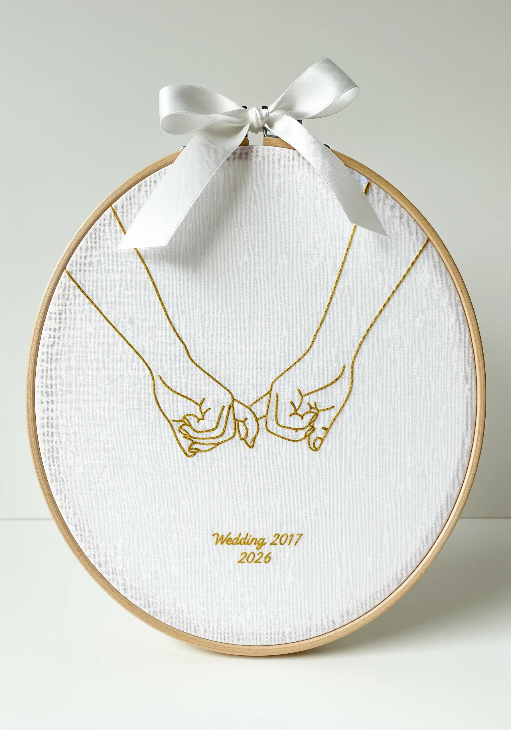 Delicate gold thread embroidery of two hands making a pinky promise on white fabric.
