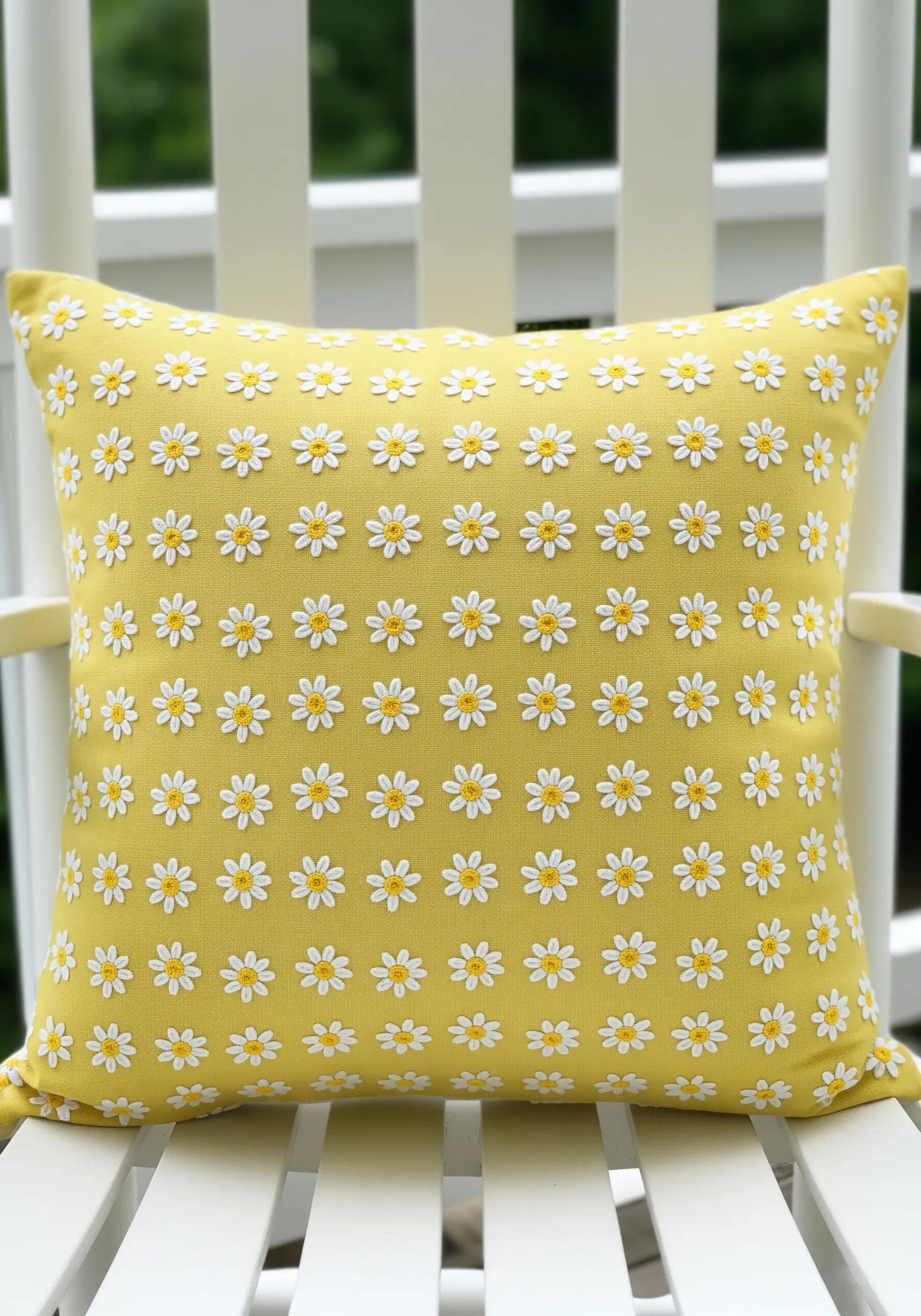 A repeating pattern of small embroidered daisies on a bright yellow pillow.