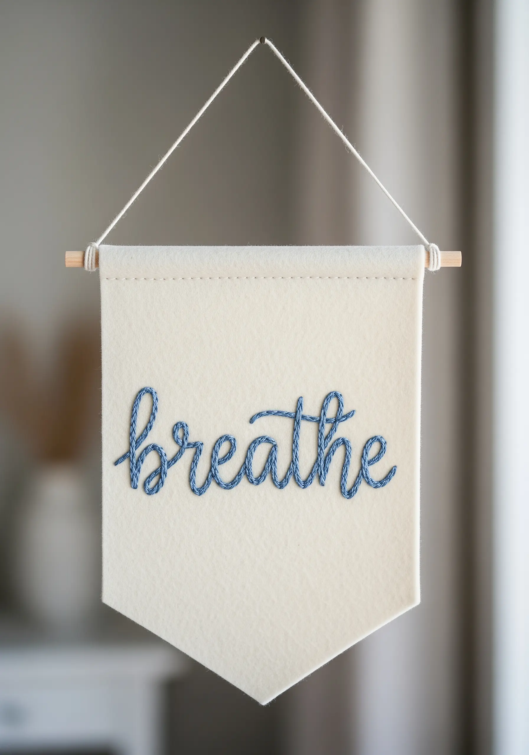 A felt wall banner with the word 'breathe' stitched in blue chain stitch.