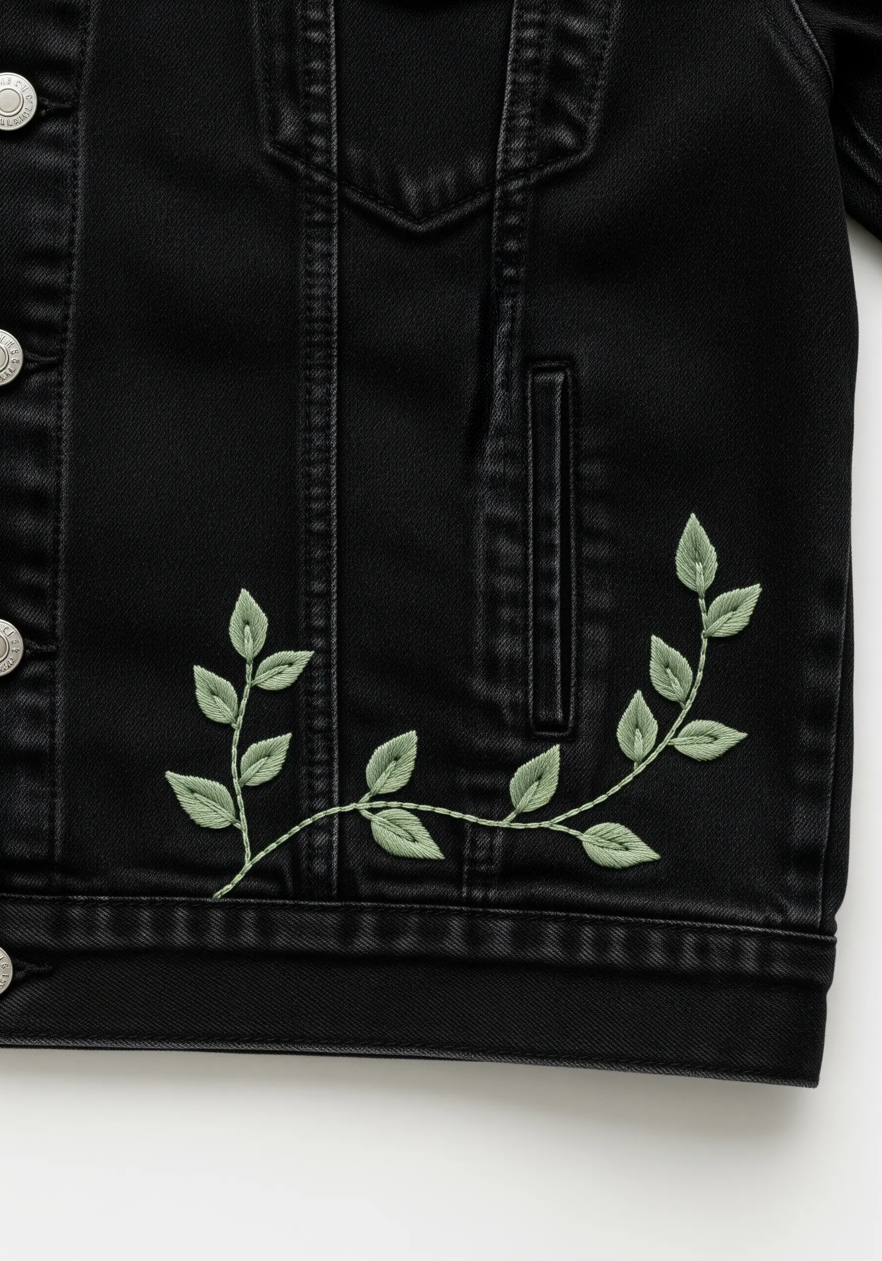 A delicate vine with sage green leaves embroidered on the front of a black denim jacket.