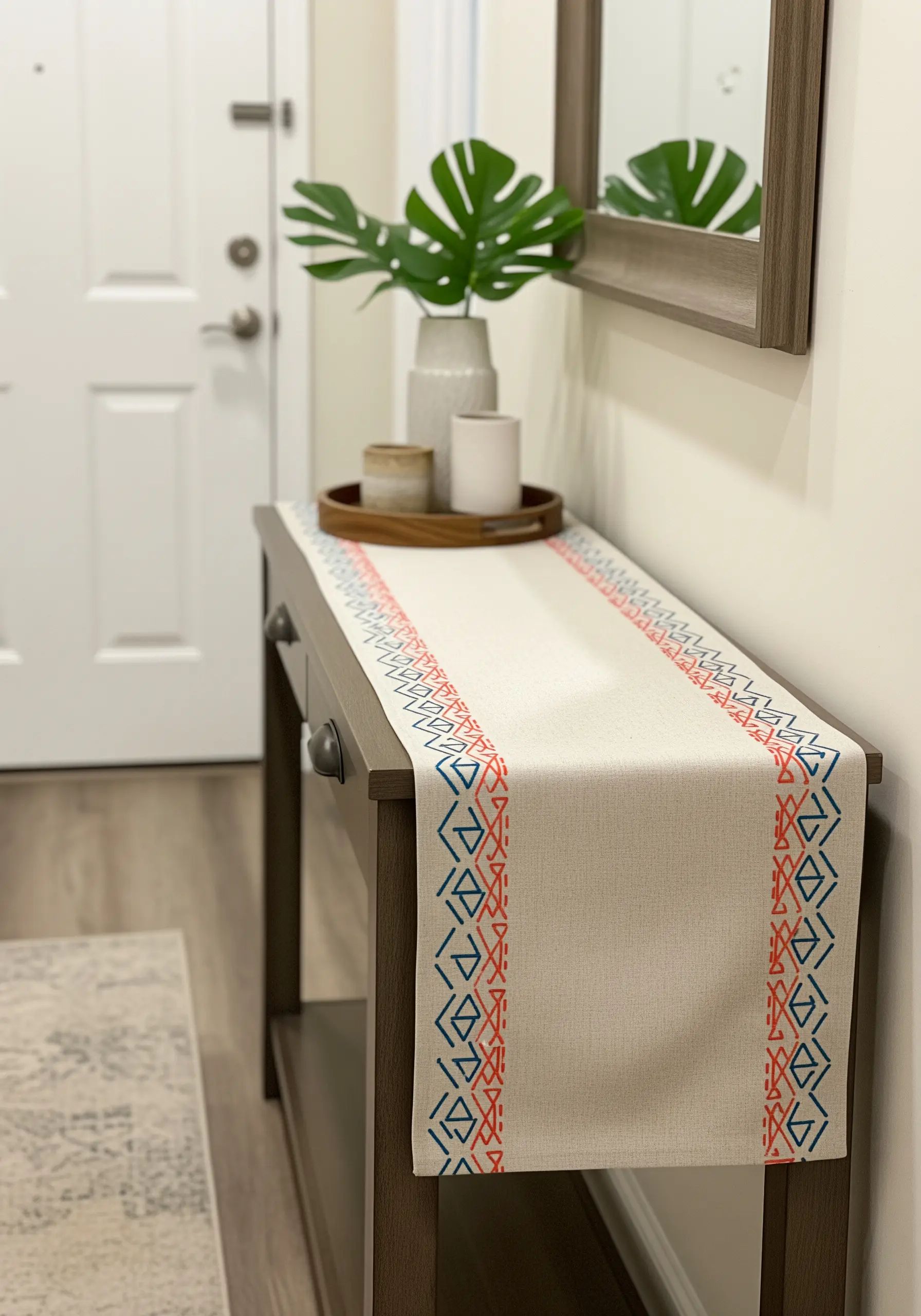 A neutral table runner on an entryway console table with a modern geometric embroidered border