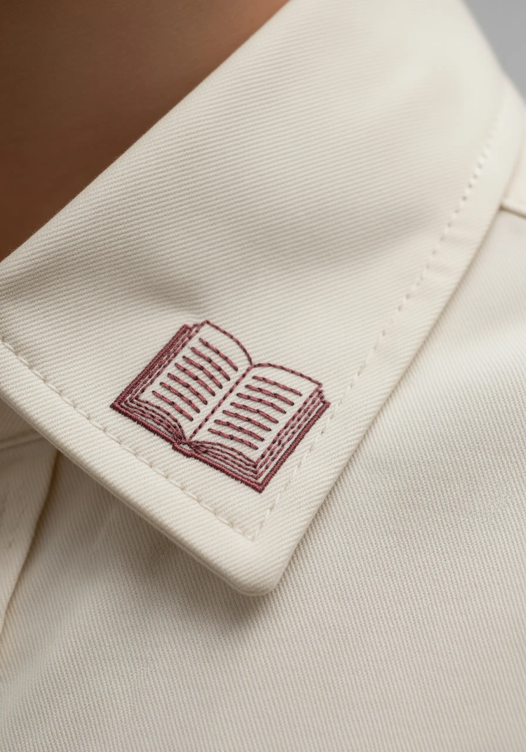 A tiny embroidered book stitched onto the corner of a shirt collar.