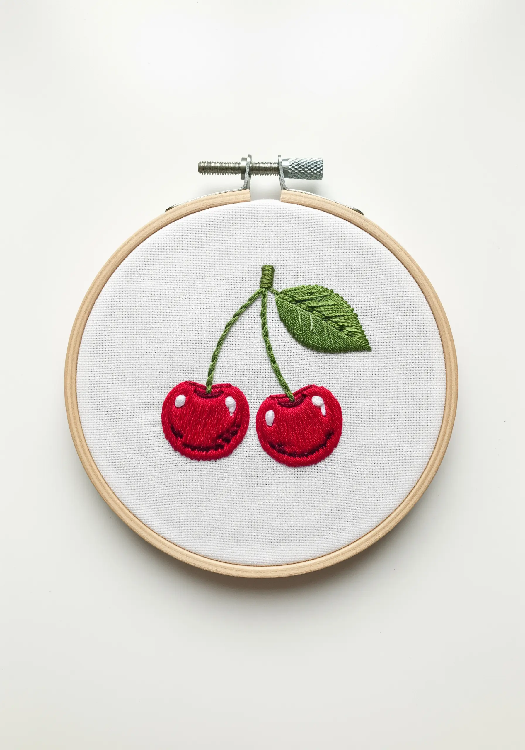 Two red embroidered cherries with green stems and leaves, each with a white highlight stitch.