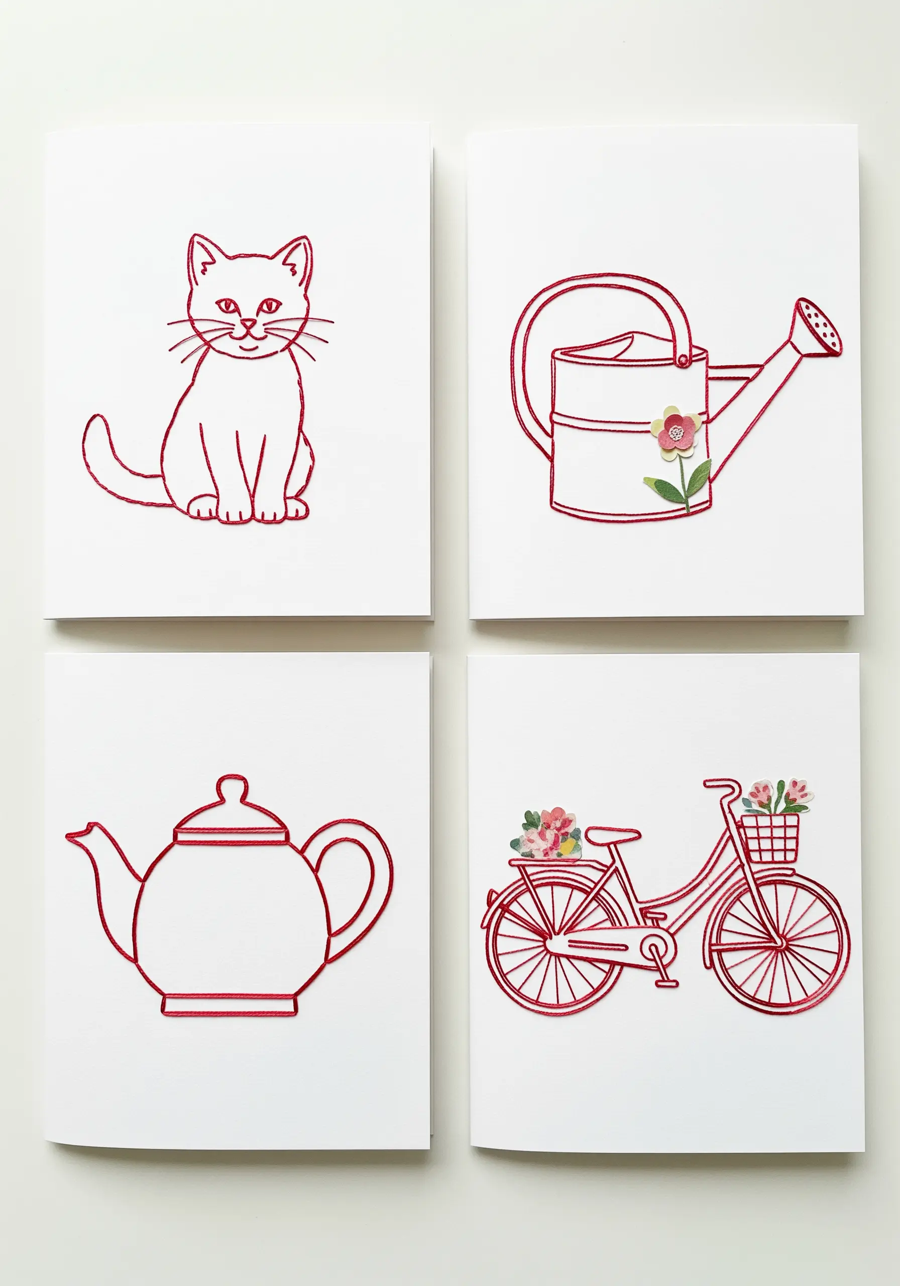 Four cards with red line drawings; one, a bicycle, has a tiny embroidered bouquet in its basket.