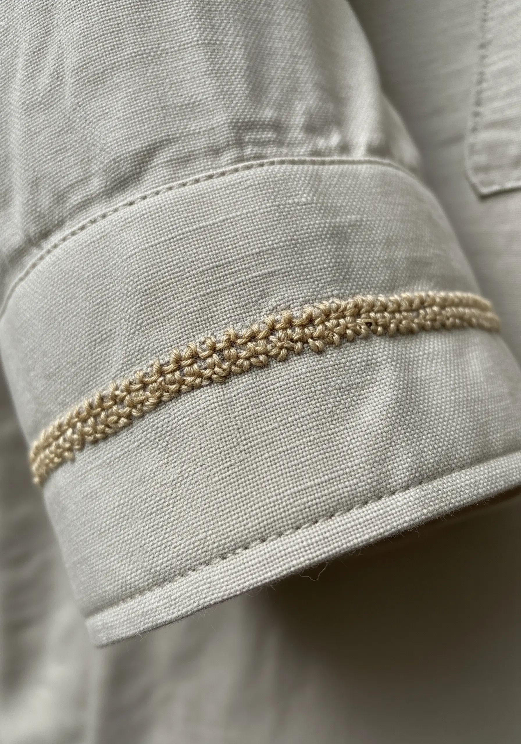 A close-up of a shirt cuff with a narrow, decorative band of beige embroidery.