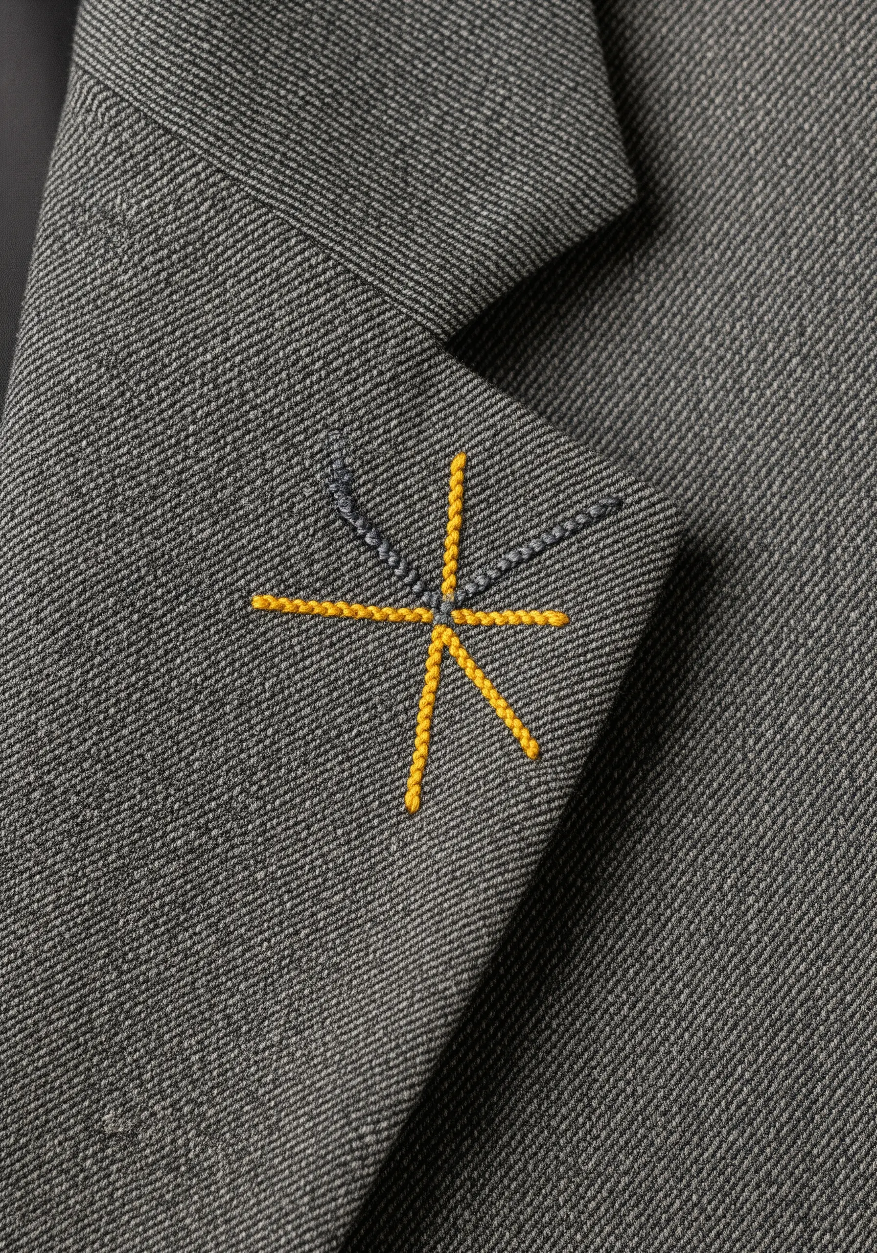 A minimalist yellow and gray asterisk-like star embroidered on the lapel of a gray blazer.