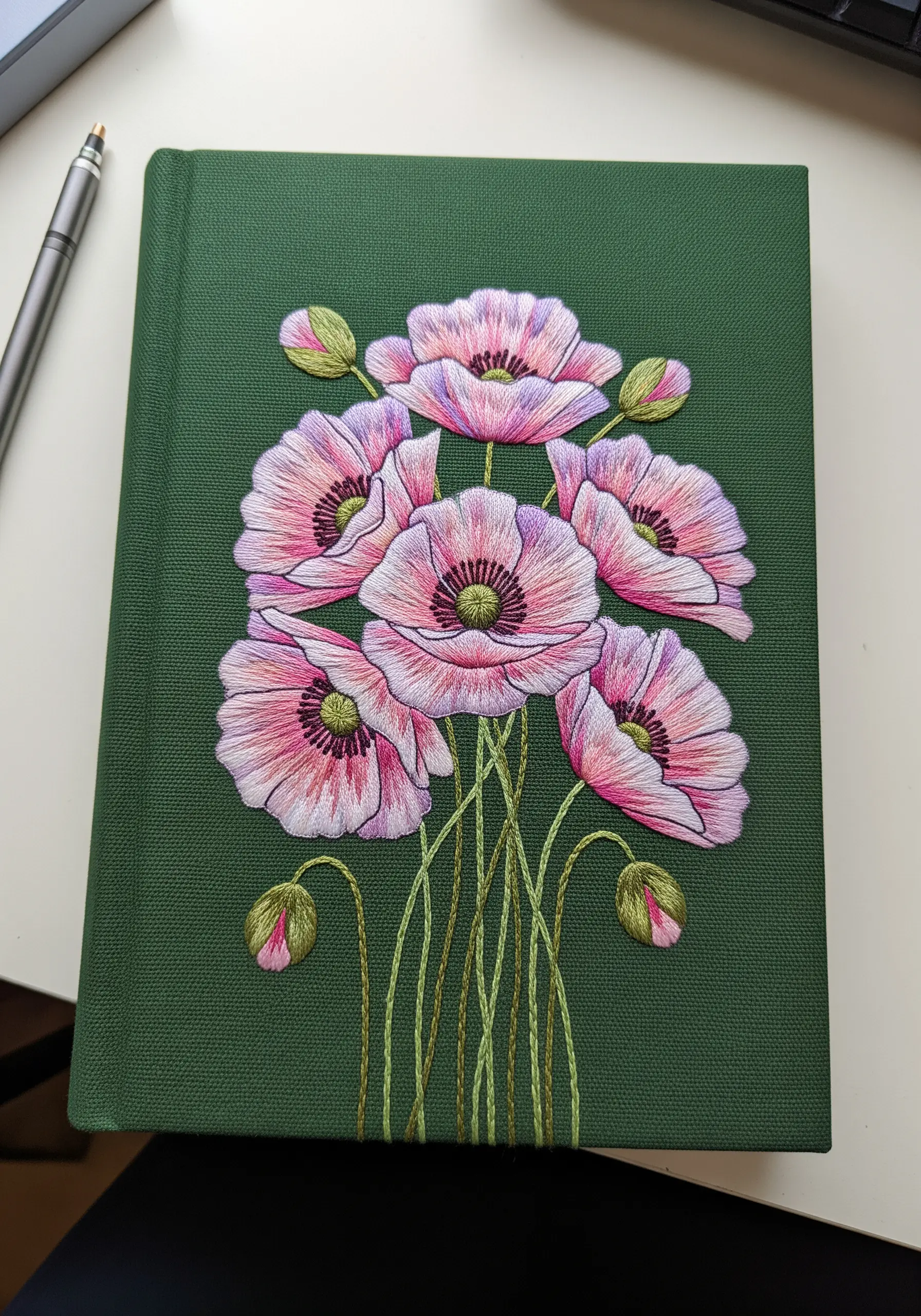 A bouquet of pink poppies with detailed thread painting on a green cloth-bound journal.