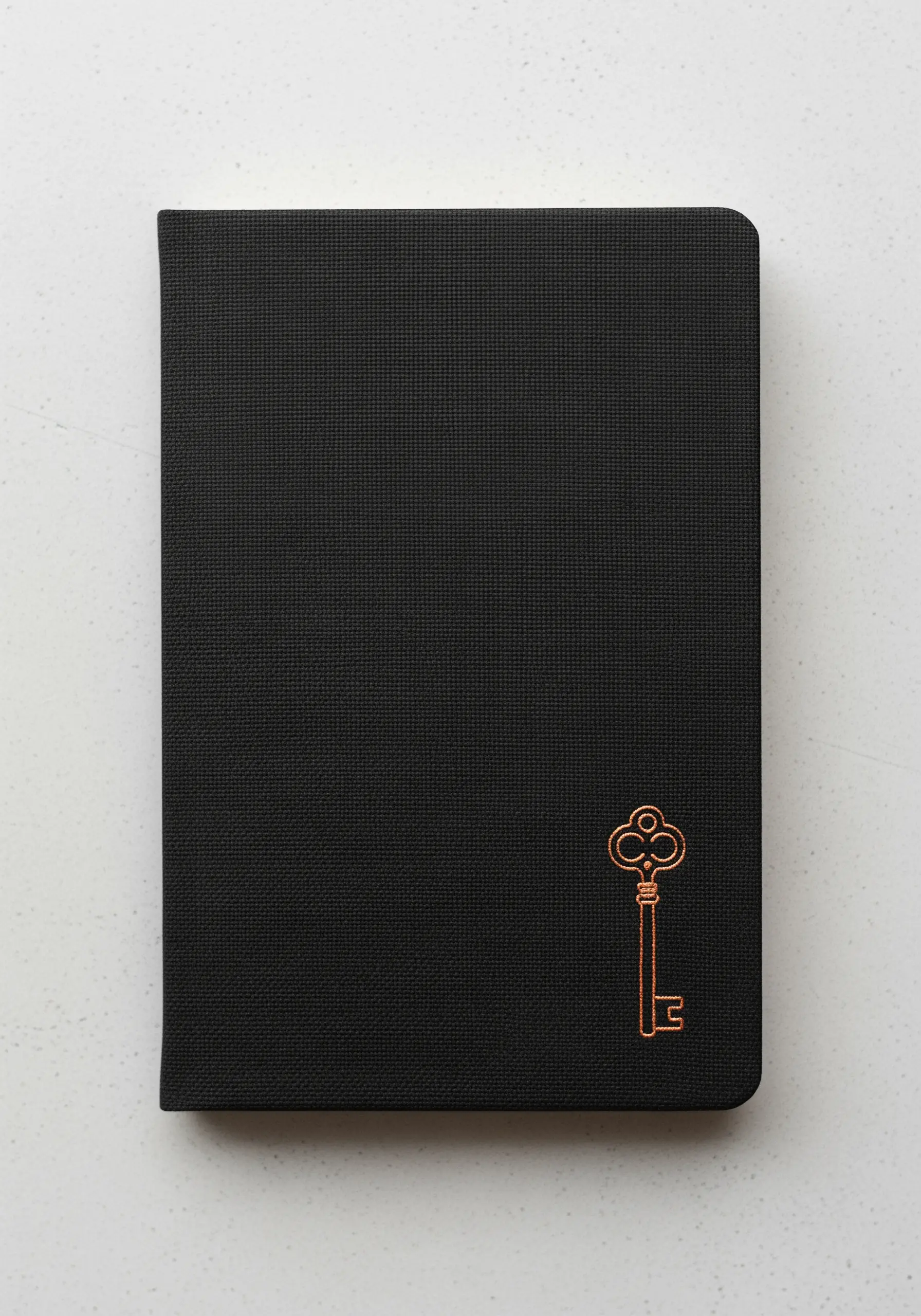 An elegant, copper metallic thread key embroidered on the corner of a black notebook.