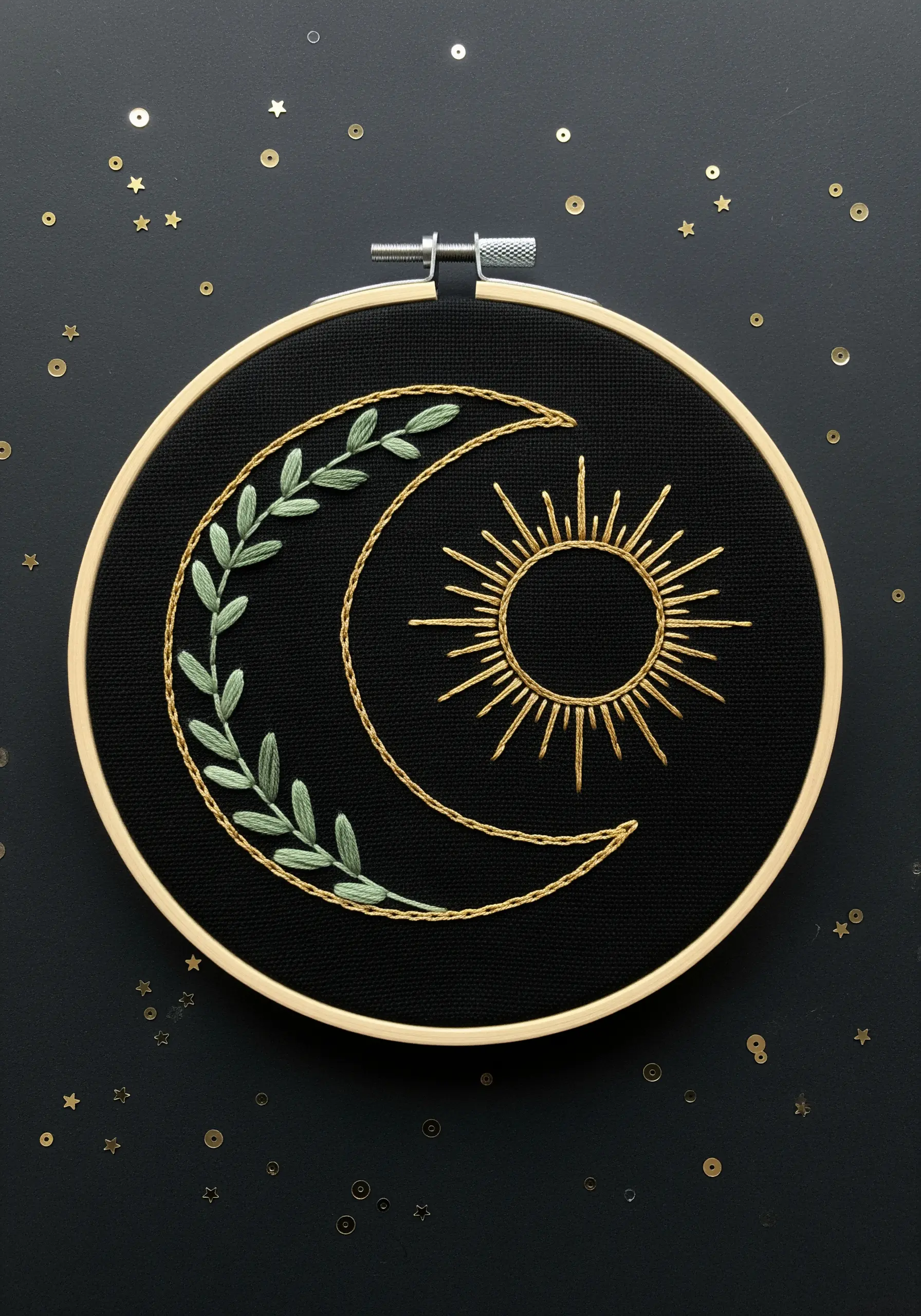 Celestial embroidery of a sun and moon with leafy vines on black fabric.