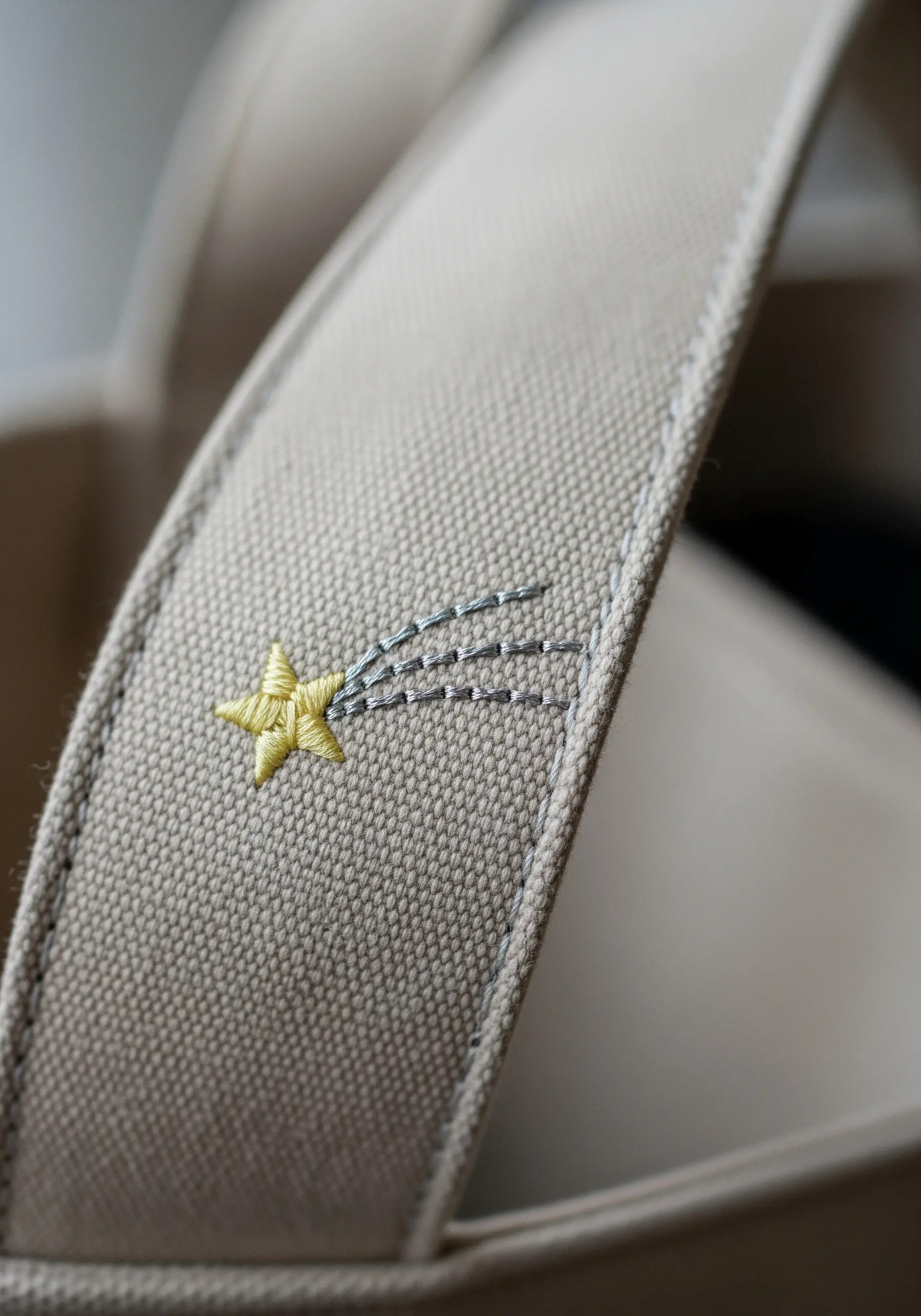 A small embroidered shooting star on the canvas strap of a tote bag.