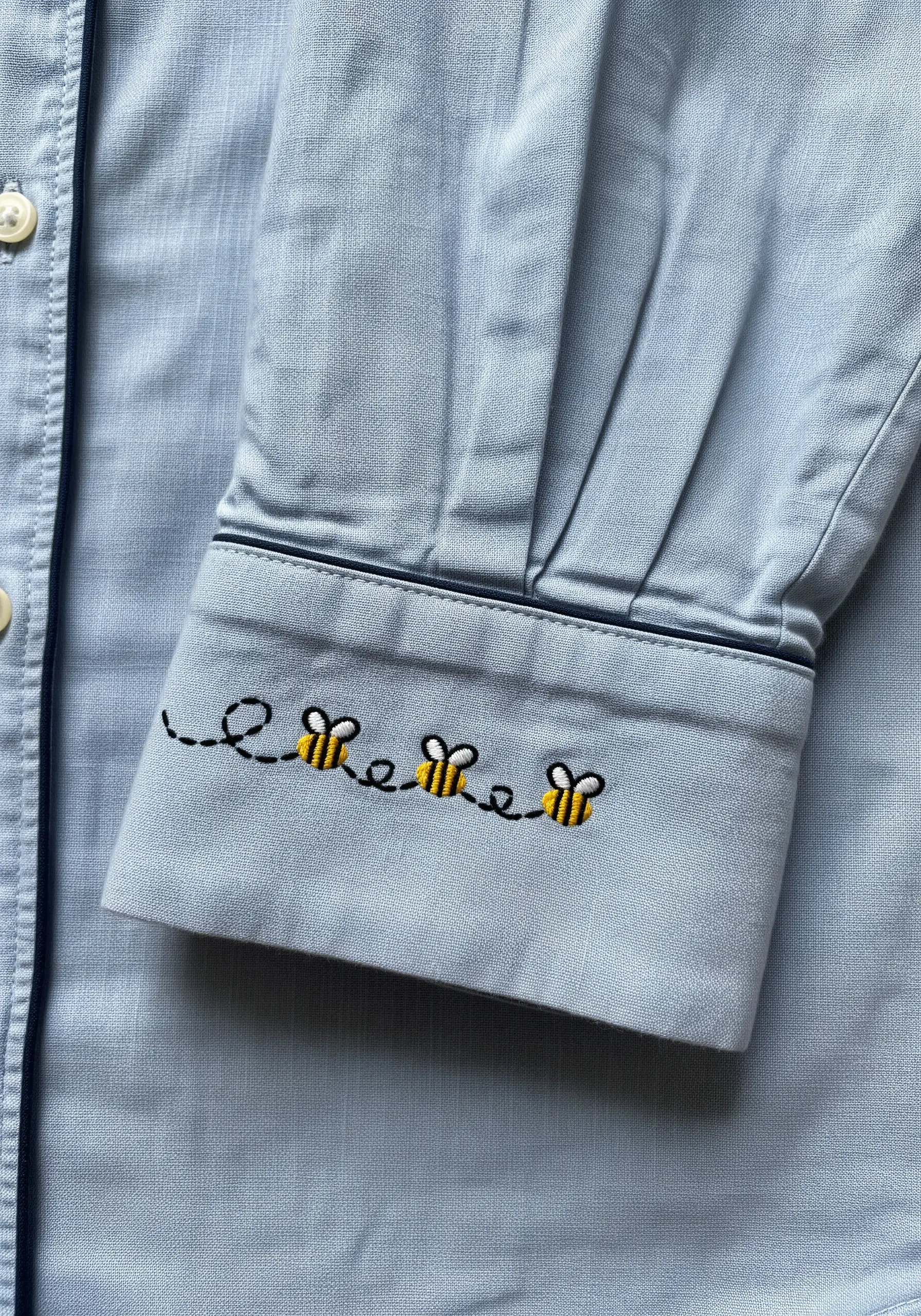 Tiny embroidered bees with a looping trail on the cuff of a blue pajama shirt.